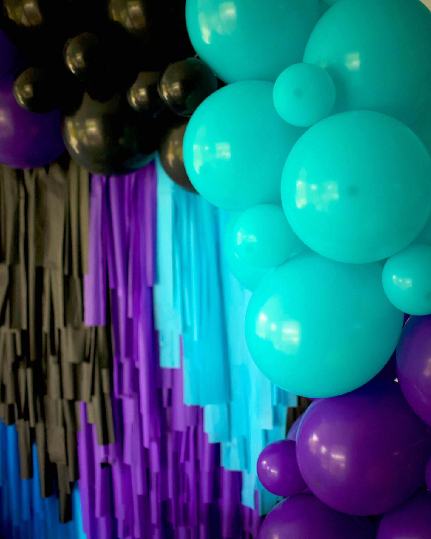 Colorful balloons in shades of teal, purple, and black, with vibrant streamers in the background.