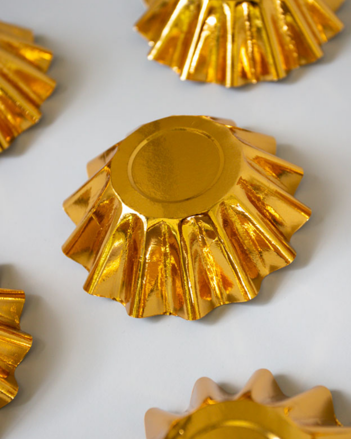 Shiny gold circular shapes with fluted edges arranged on a light surface, reflecting light and creating texture.