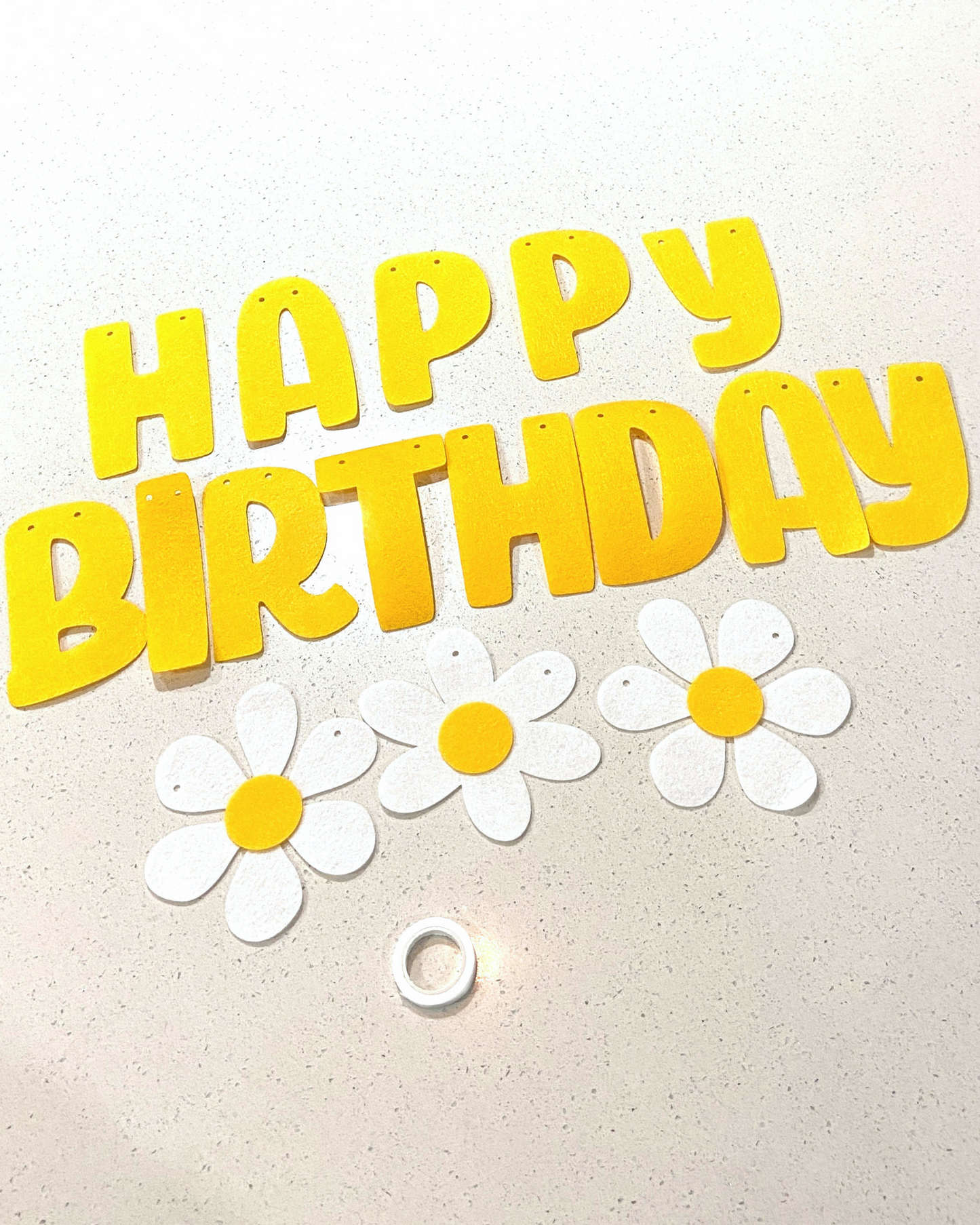 Bright yellow letters spell "HAPPY BIRTHDAY" alongside white flowers with yellow centers on a light surface.