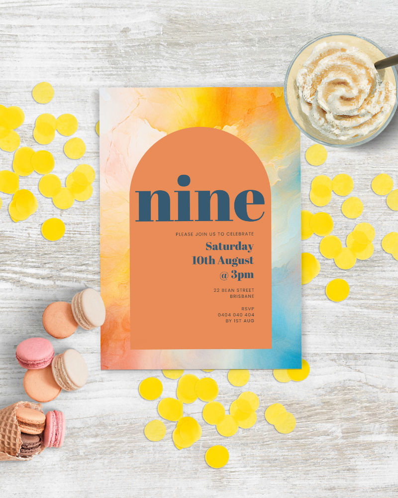 Colorful celebration invitation with confetti, macarons, and a frosty dessert on a rustic wooden surface.