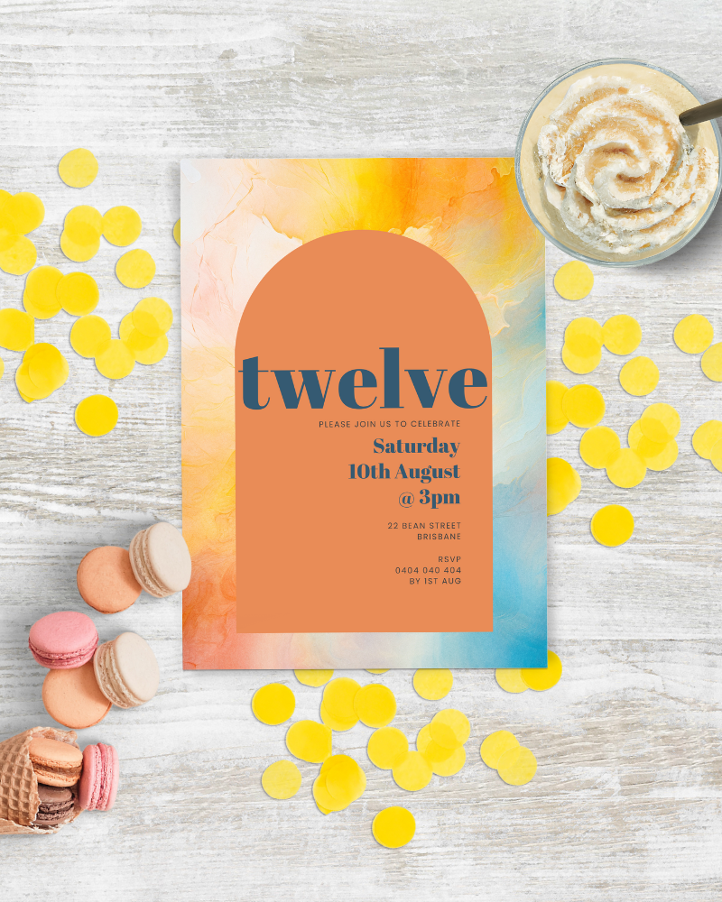 Colorful invitation featuring a peach and blue gradient with yellow confetti and macarons on a wooden surface.