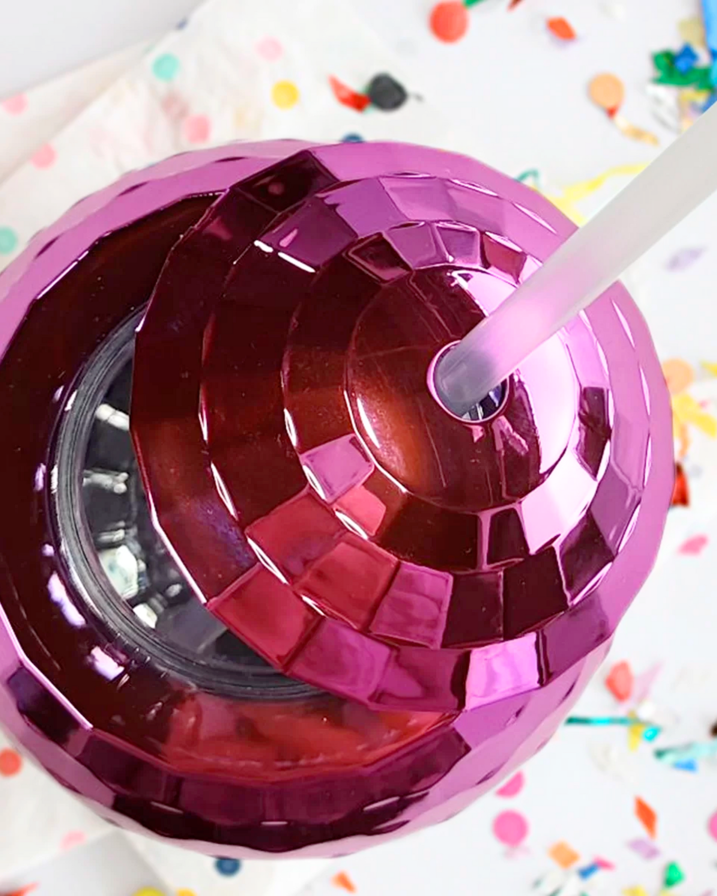 Shiny pink container with a spiral pattern and a straw, set against a colorful, confetti-like background.