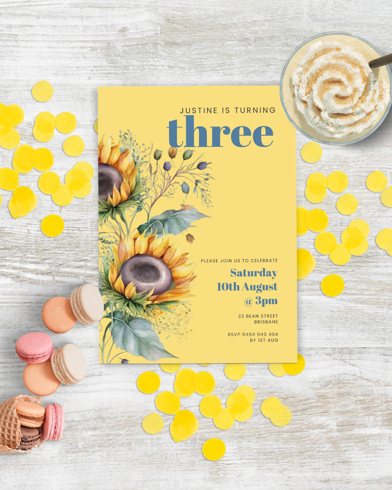 Colorful birthday invitation featuring sunflowers, yellow confetti, and sweet treats on a light wood surface.