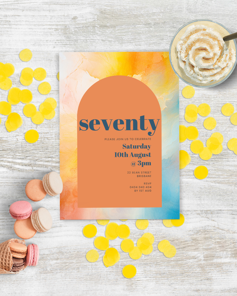 Colorful invitation with "seventy" text, surrounded by macarons, ice cream cone, and vibrant confetti on a wooden surface.