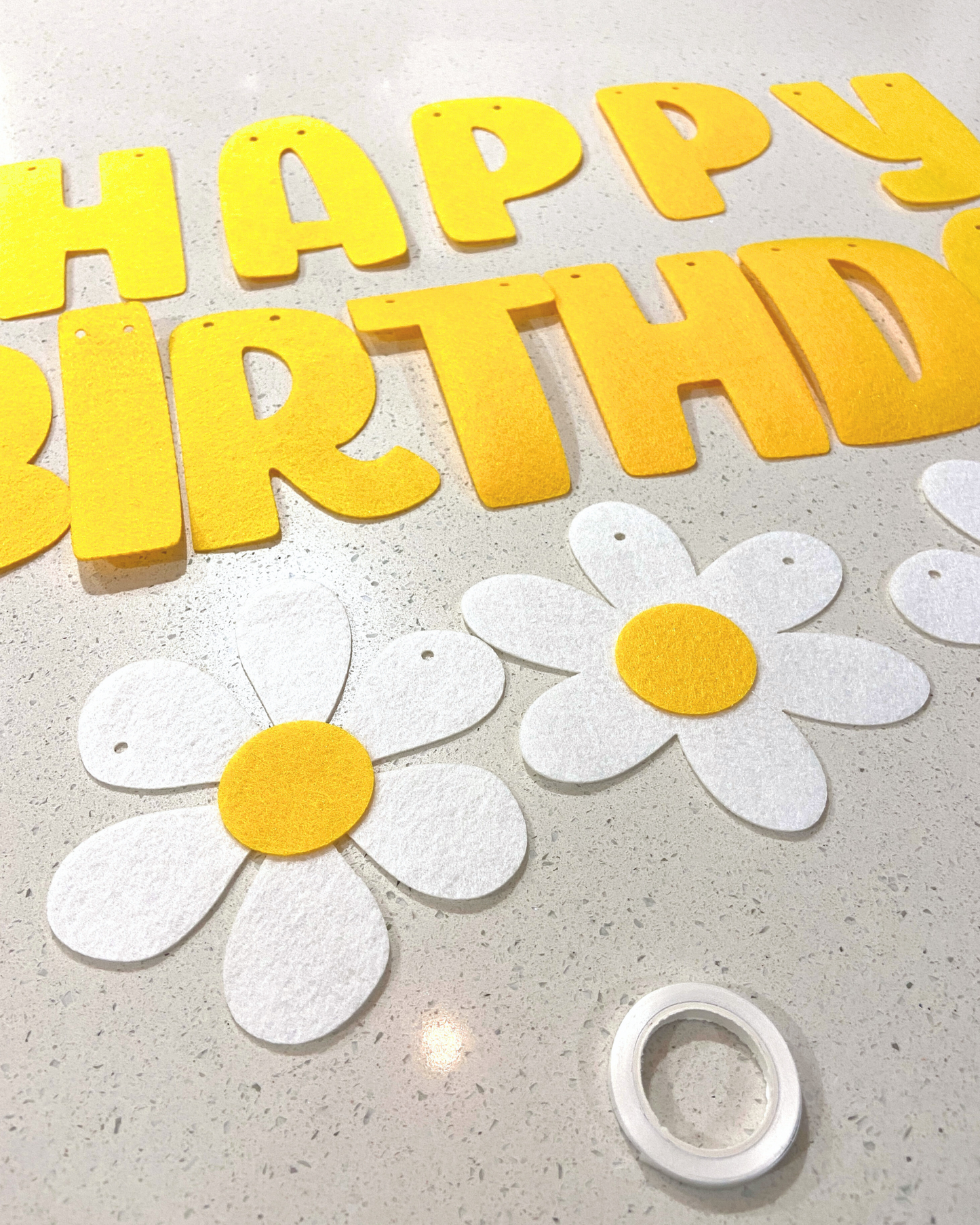 Colorful letters spell "HAPPY BIRTHDAY" alongside white flowers with yellow centers on a smooth surface.