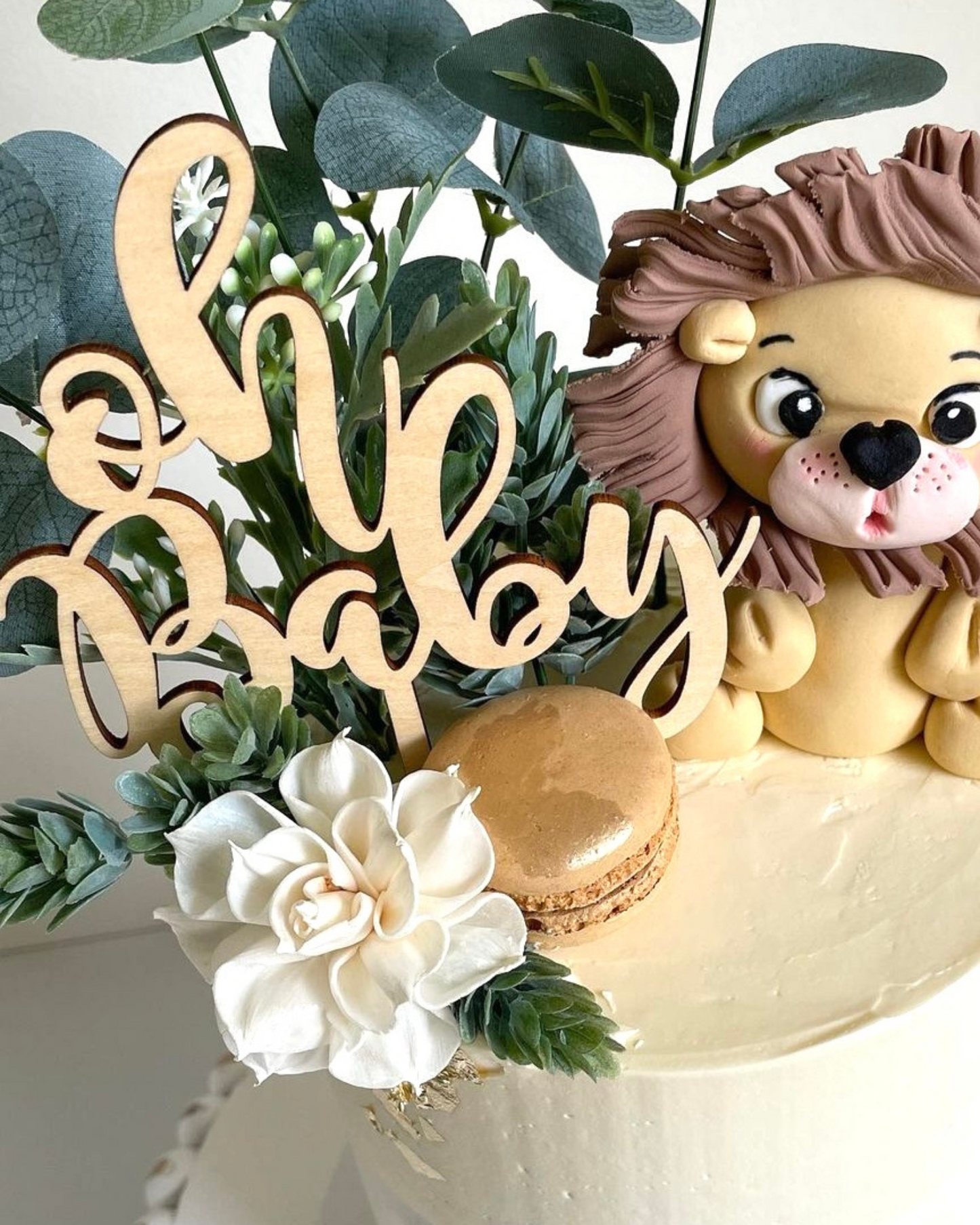 A charming lion figurine surrounded by greenery, a flower, and a golden treat, with "Oh Baby" in elegant script.