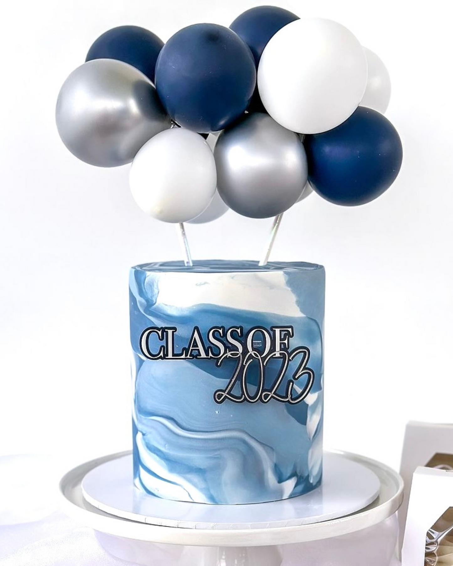 A marbled blue cake topped with silver and navy balloons, celebrating the Class of 2023.