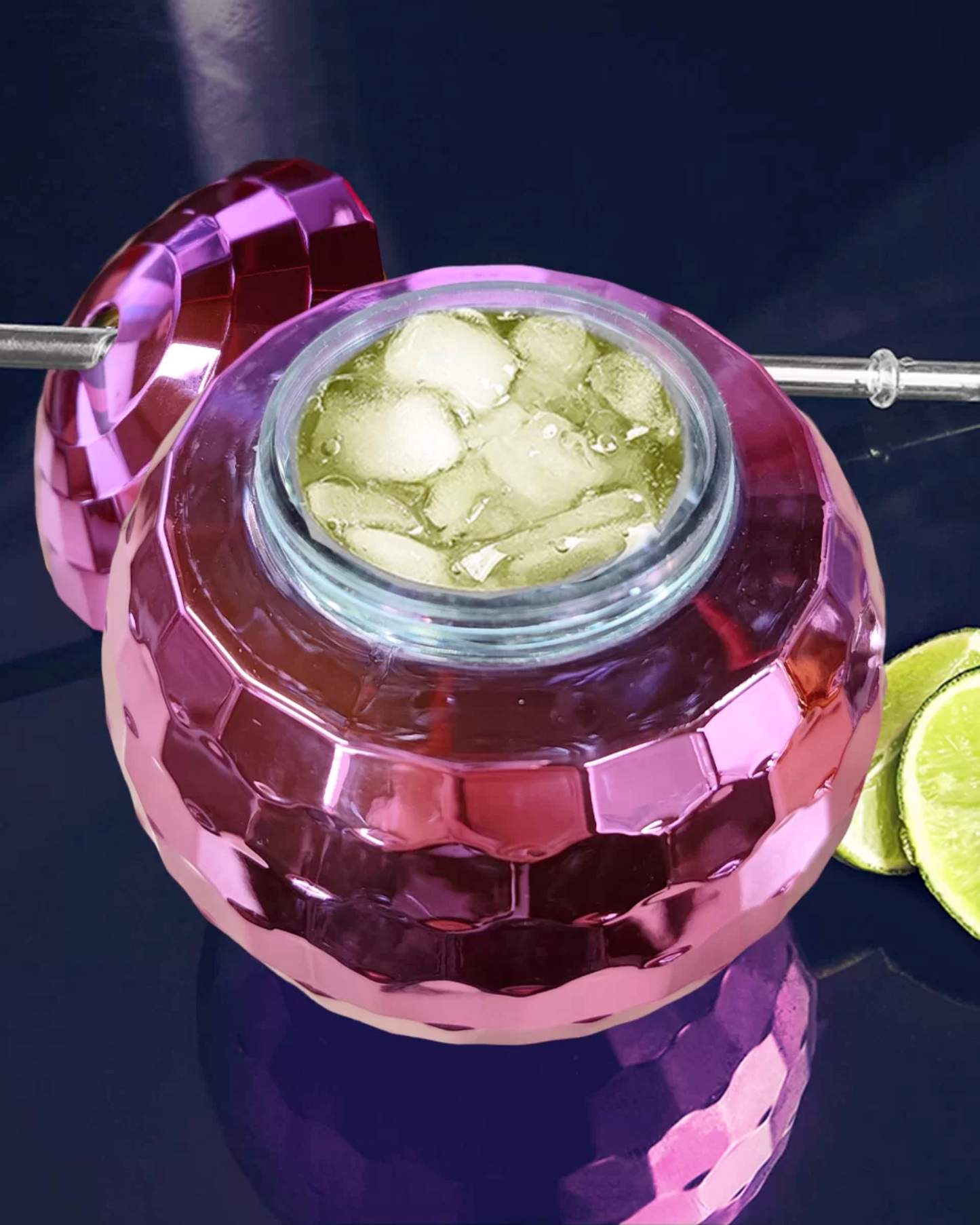 A vibrant pink container filled with ice and a refreshing beverage, accompanied by lime slices on a reflective surface.