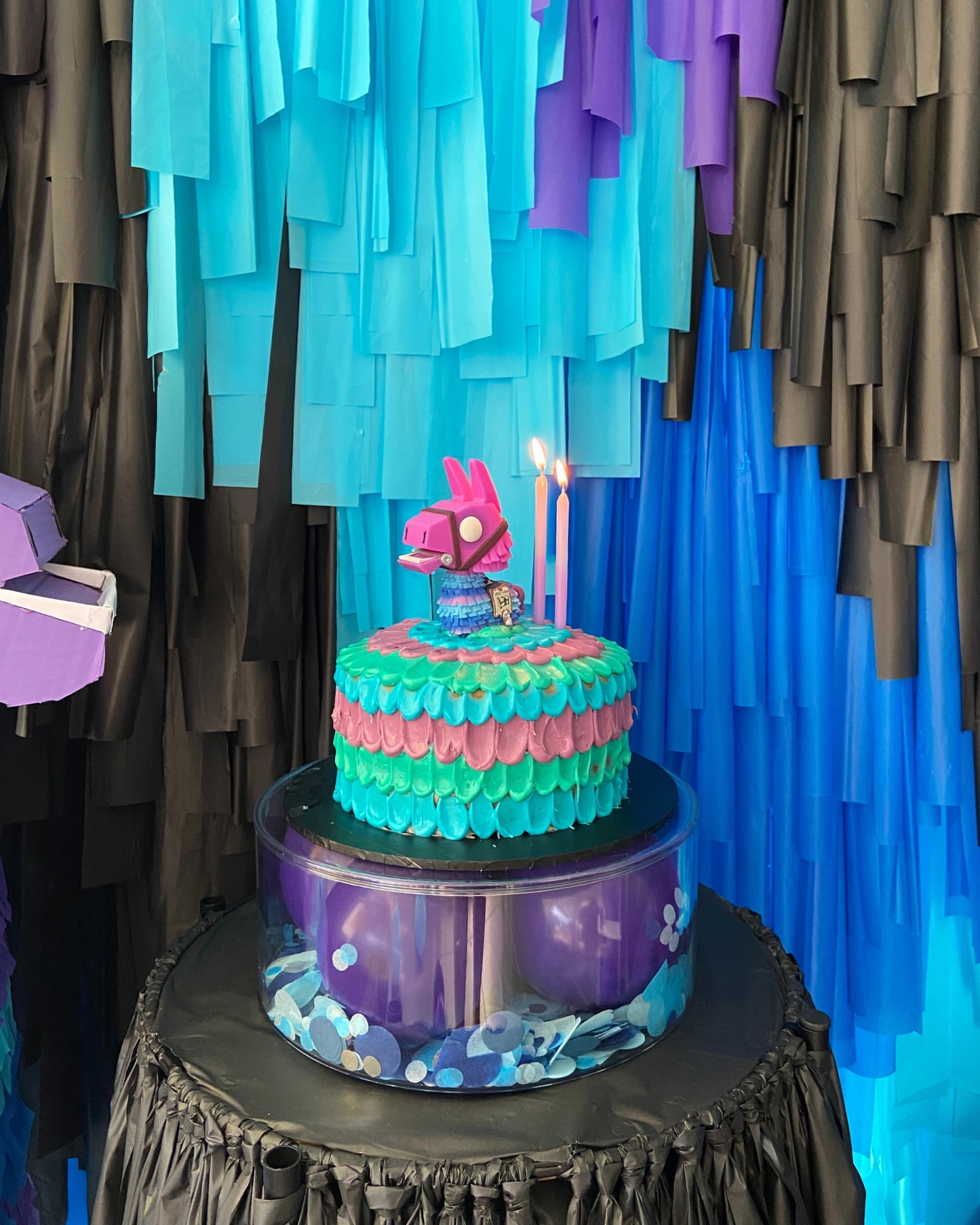 A colorful cake topped with a playful figure, surrounded by vibrant streamers and two lit candles.
