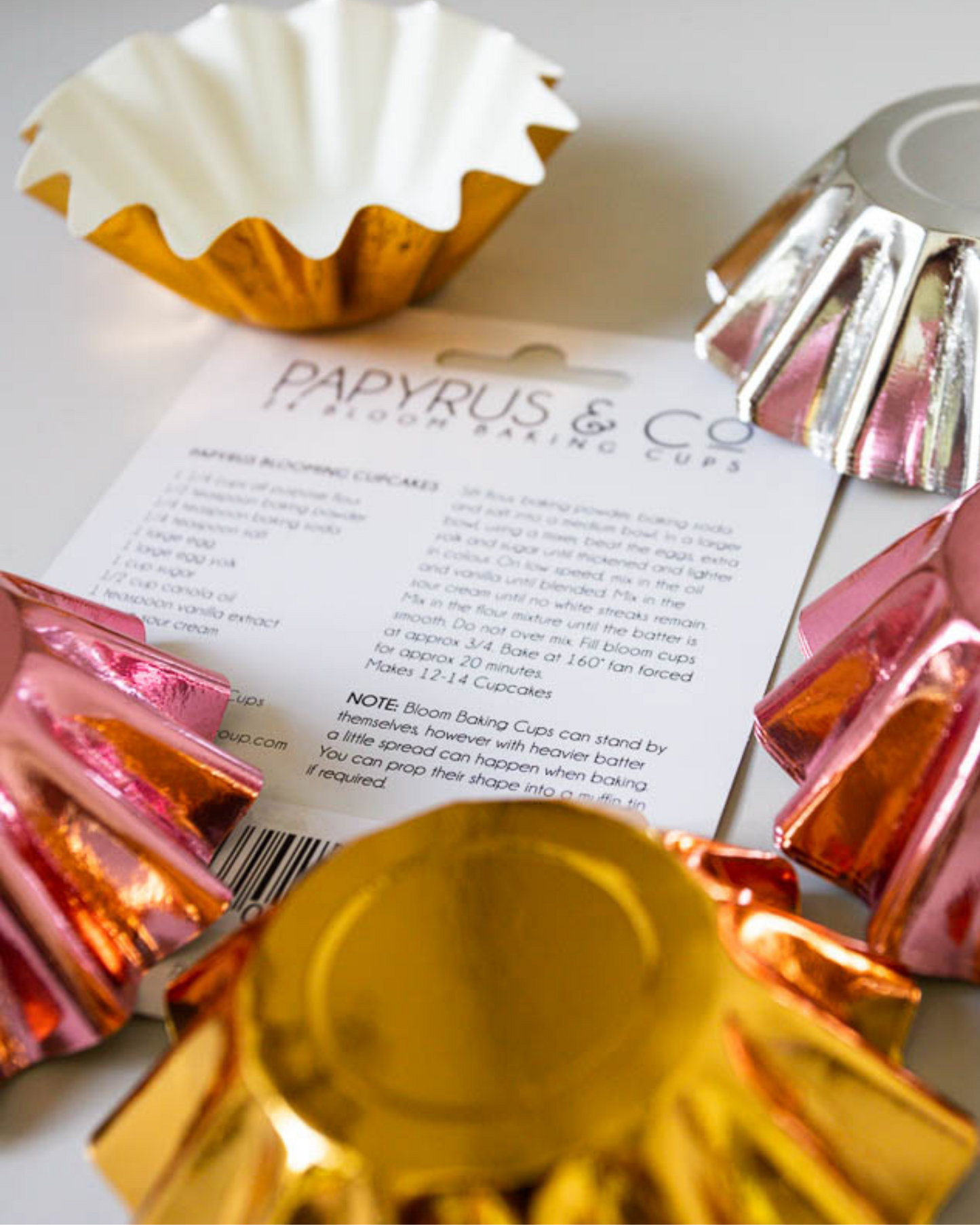 Colorful, fluted baking cups in gold, silver, and pink arranged around a recipe card with instructions and notes.