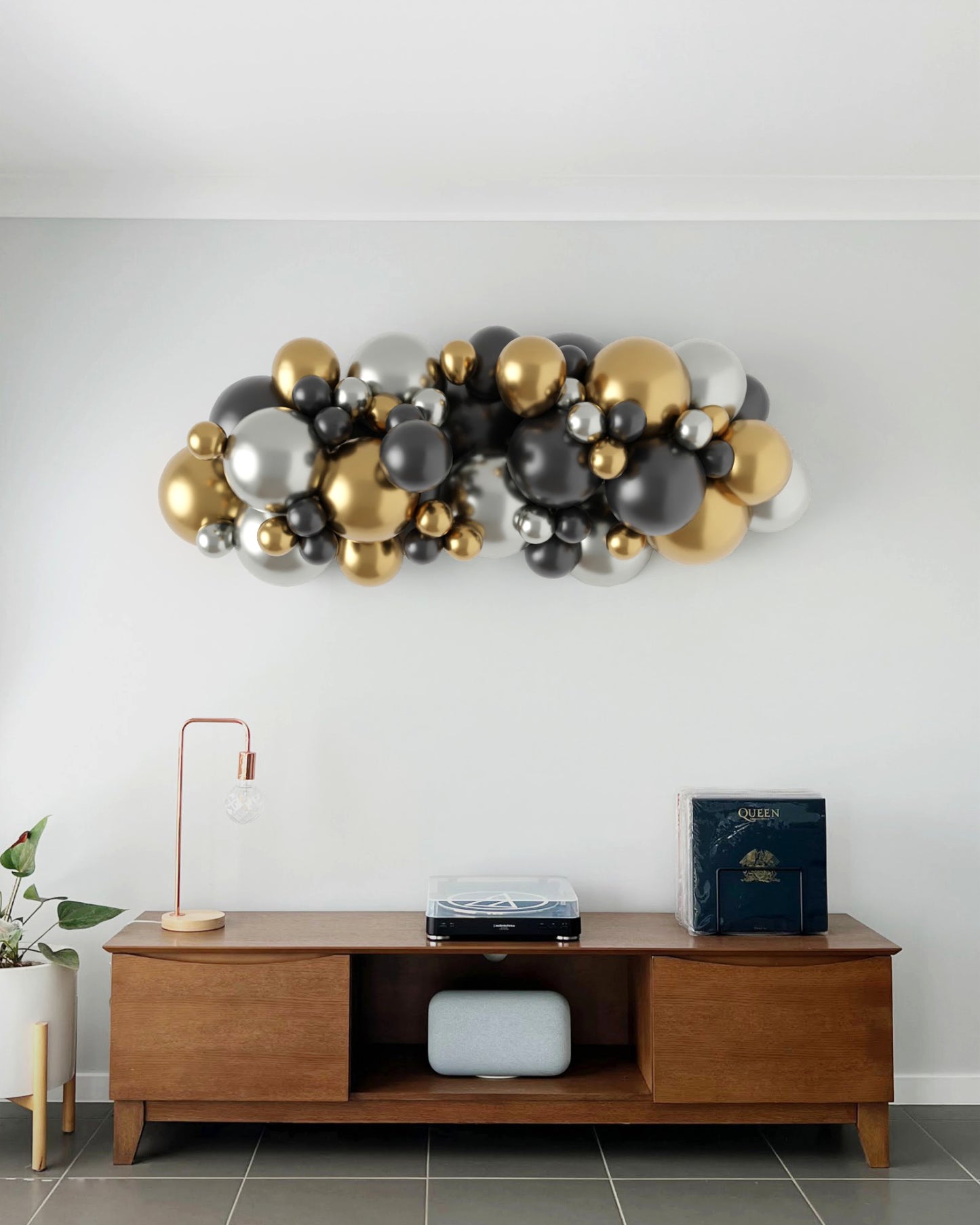 A vibrant arrangement of black, silver, and gold balloons mounted on a wall above a stylish wooden console table.