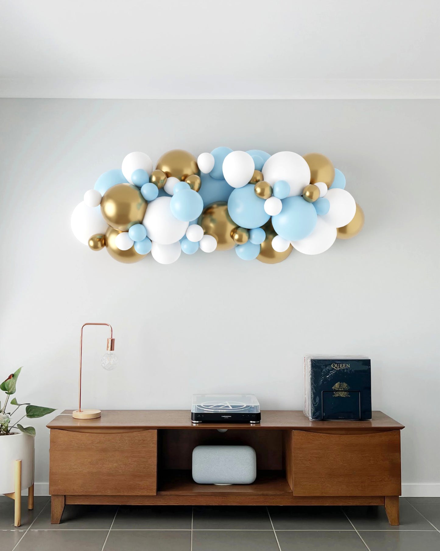 A vibrant balloon garland in blue, white, and gold decorates a light wall above a stylish wooden console table.