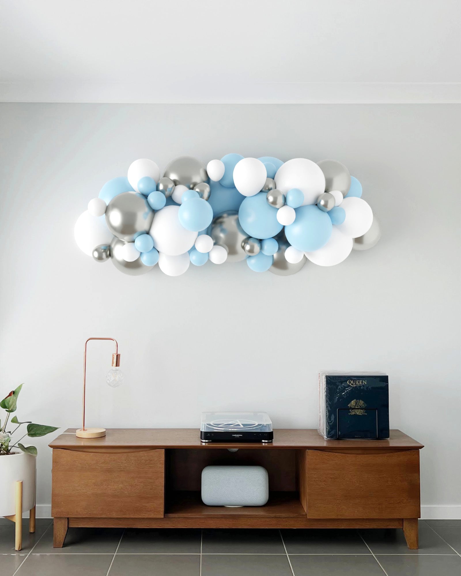 A colorful balloon garland in blue, white, and silver decorates a modern living space above a wooden console table.