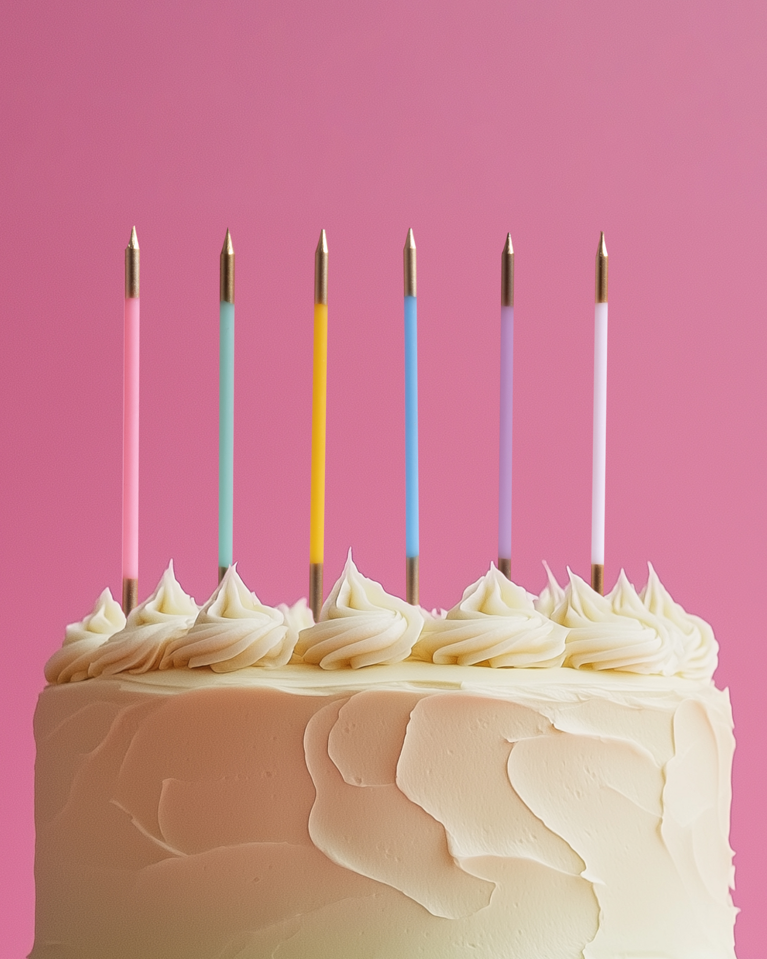 A pastel cake topped with swirls of cream and colorful candles against a bright pink background.