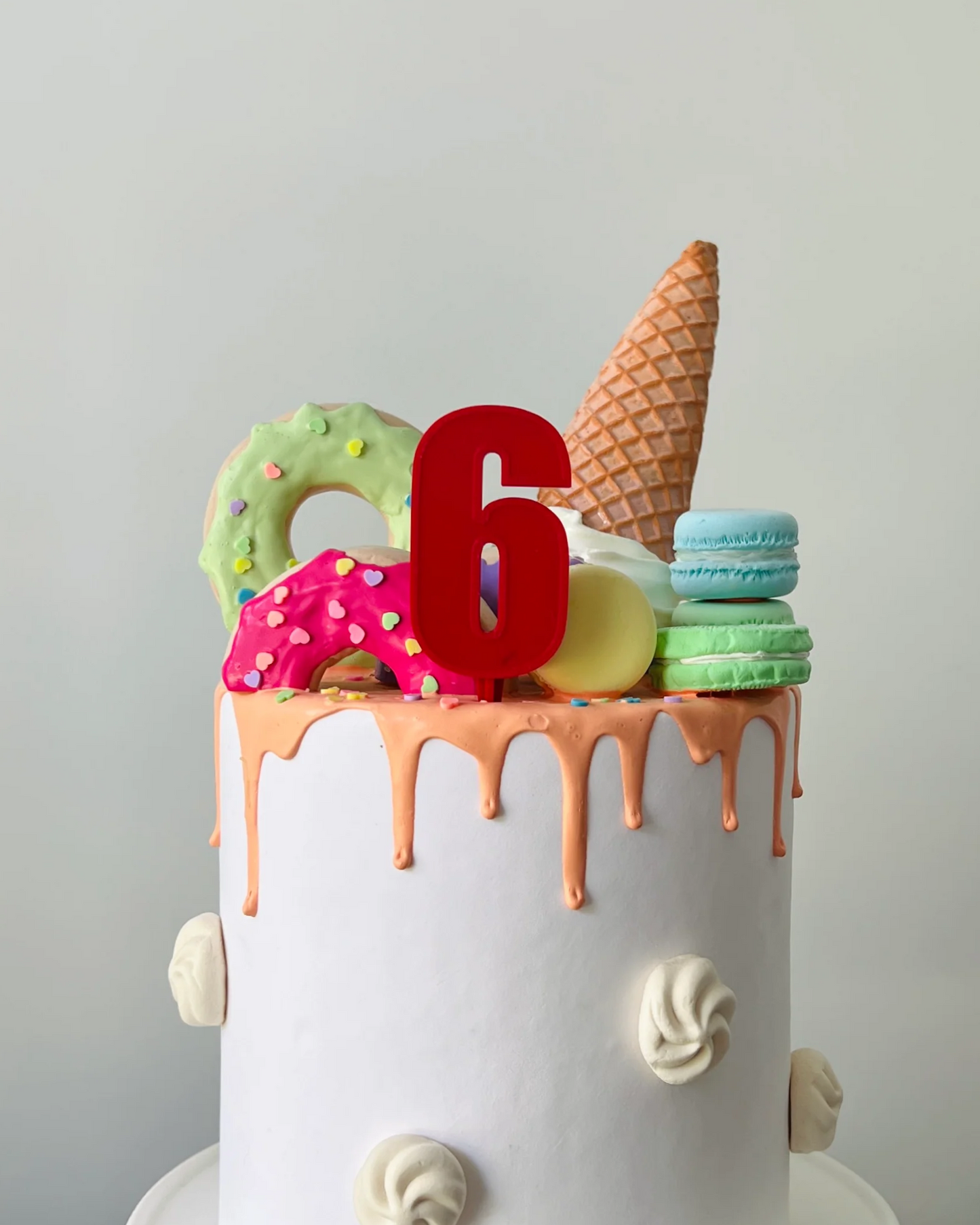 A white cake topped with colorful decorations, including a red number 6, ice cream cone, and assorted sweets.