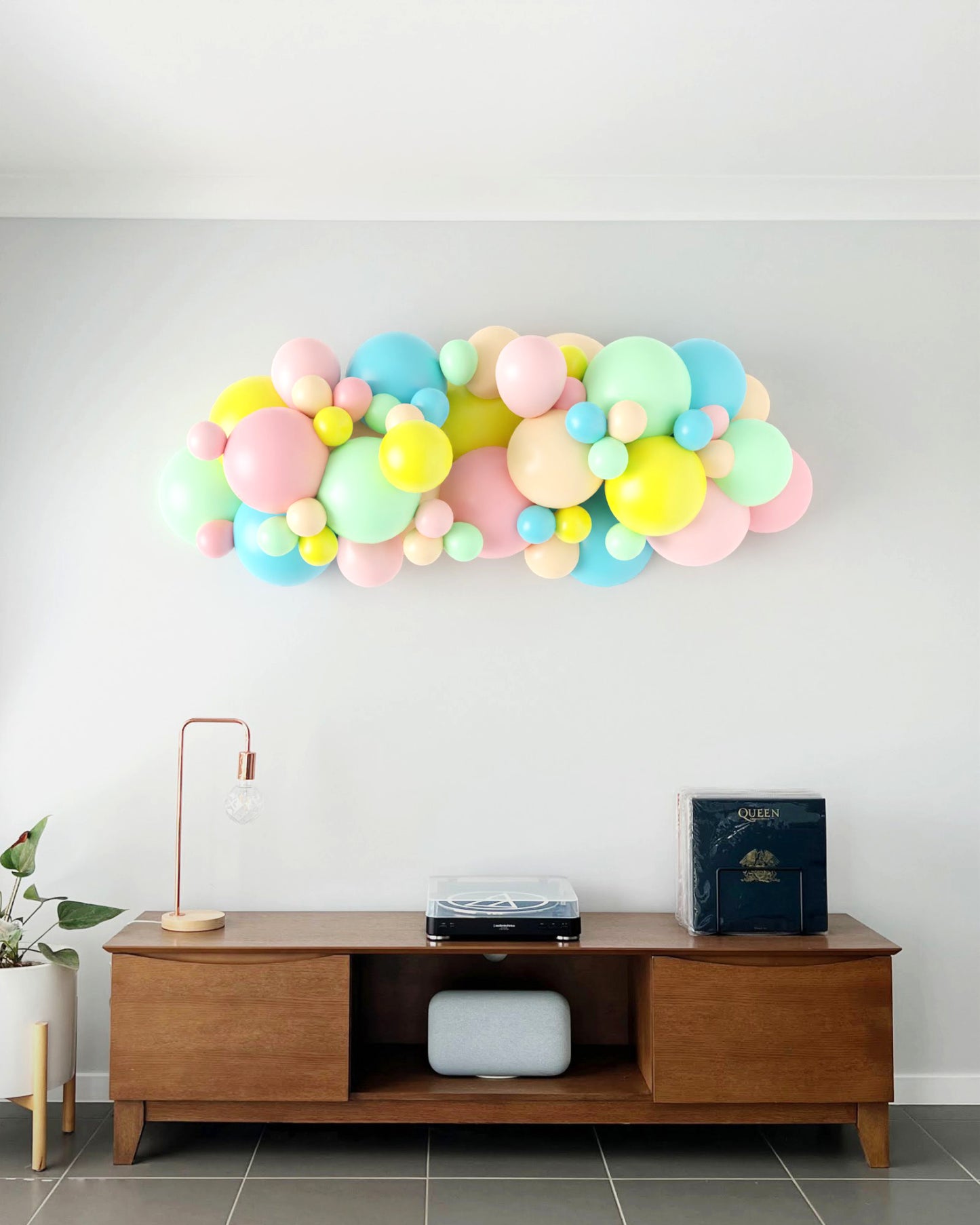 A colorful balloon garland in pastel hues adorns a wall above a stylish wooden console table and modern decor.