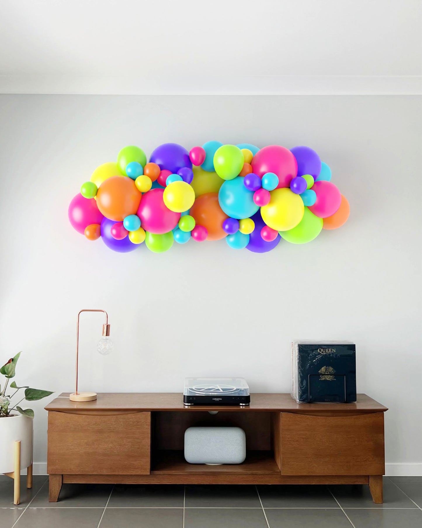 Colorful balloon garland in vibrant hues of pink, purple, green, and blue, mounted above a wooden sideboard.