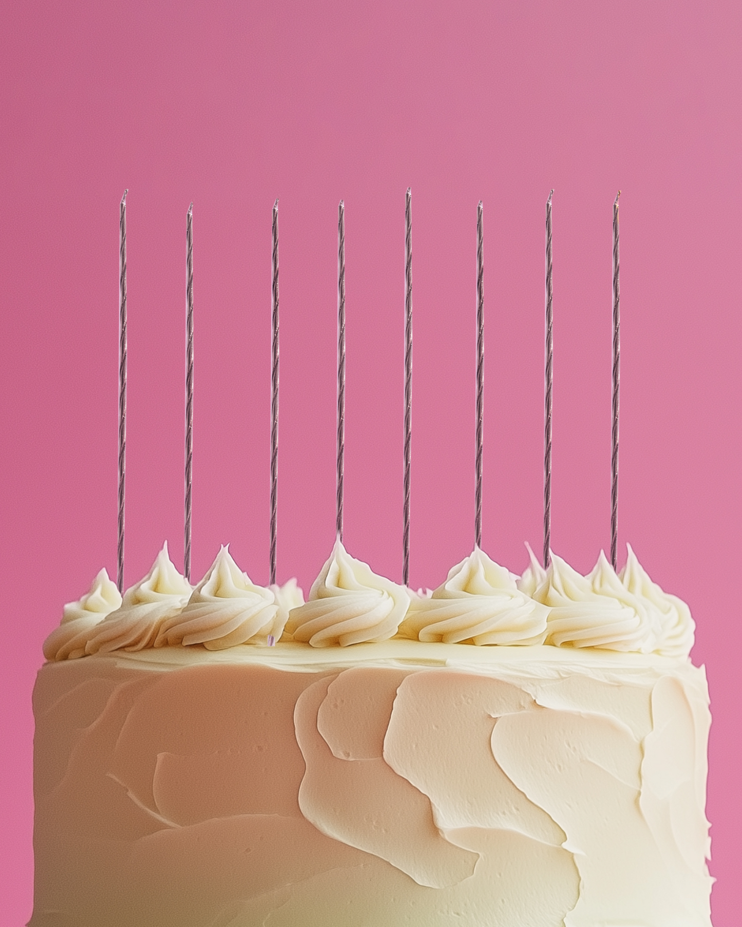 Tall layered cake with creamy frosting topped by nine twisted candles against a vibrant pink background.