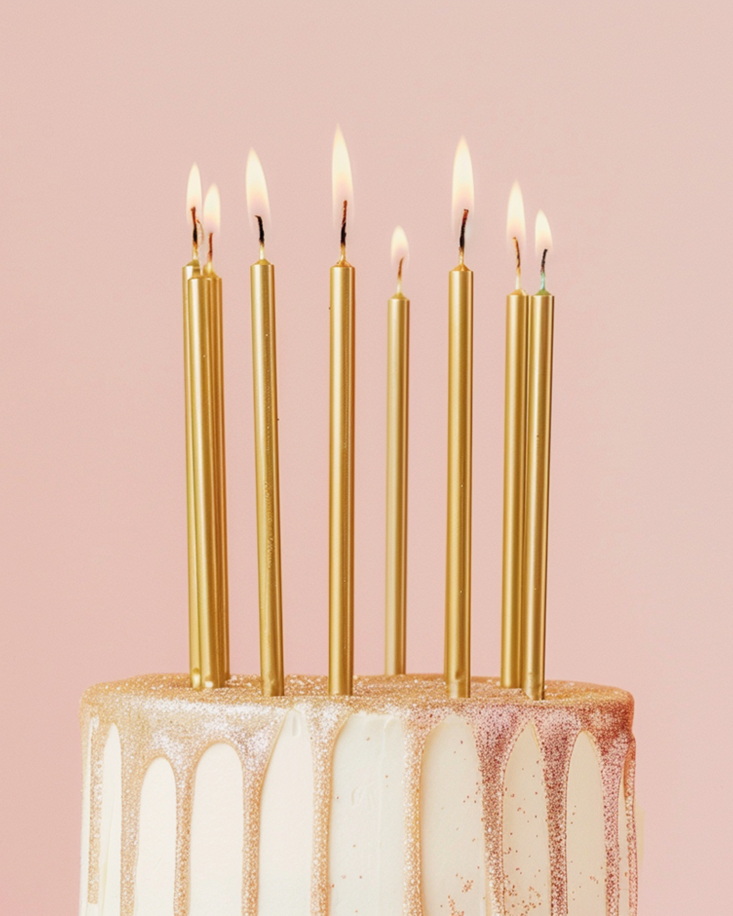 Golden candles with flames atop a decorated cake, set against a soft pink background.