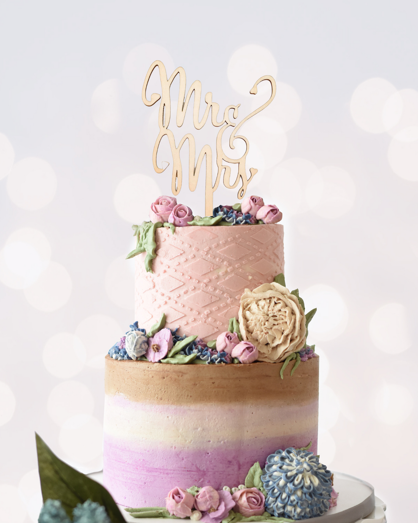 A beautifully decorated three-tier cake with pastel colors, floral accents, and a "Mr & Mrs" topper.