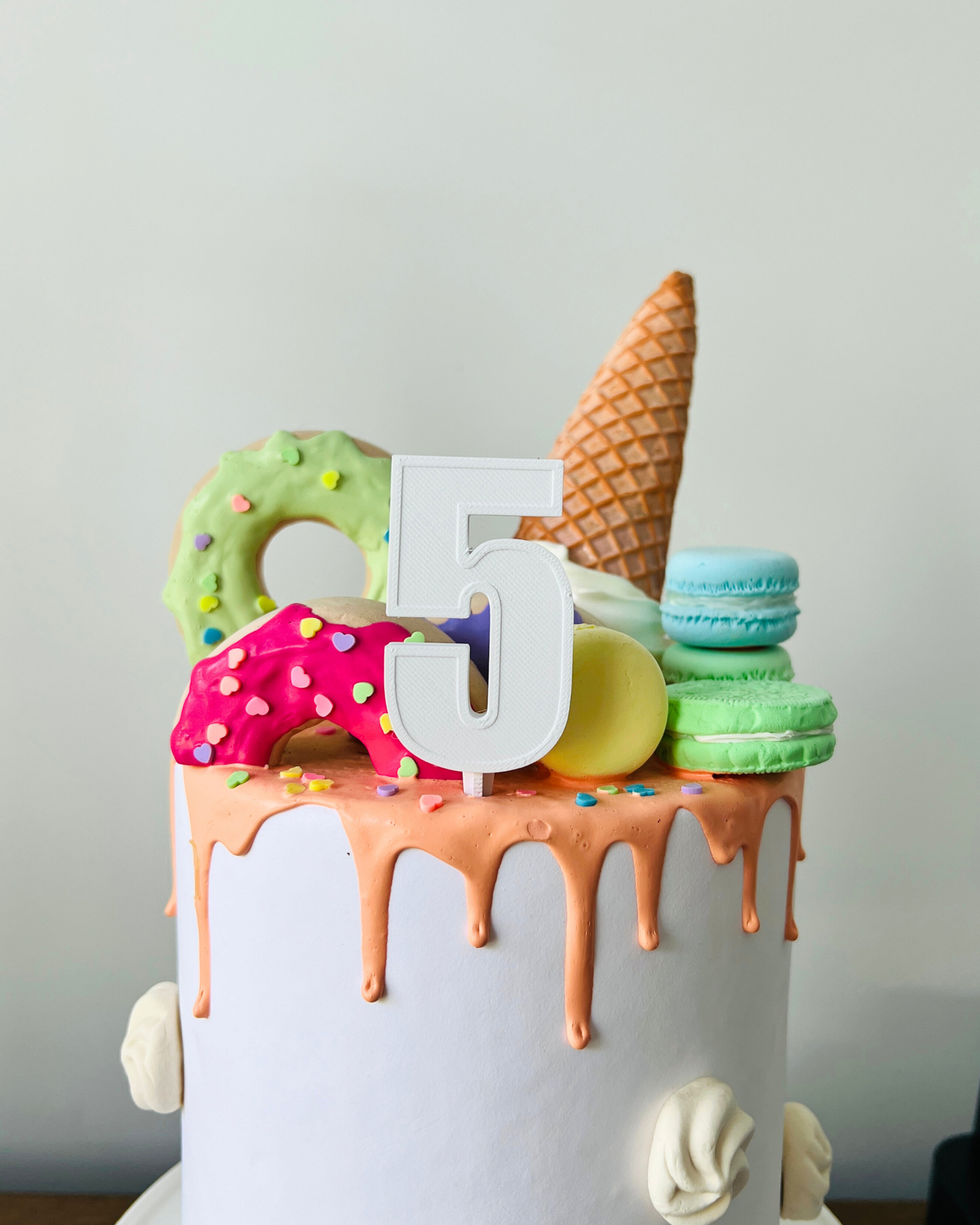 Colorful cake topped with a white number 5, ice cream cone, macarons, and decorated donuts.