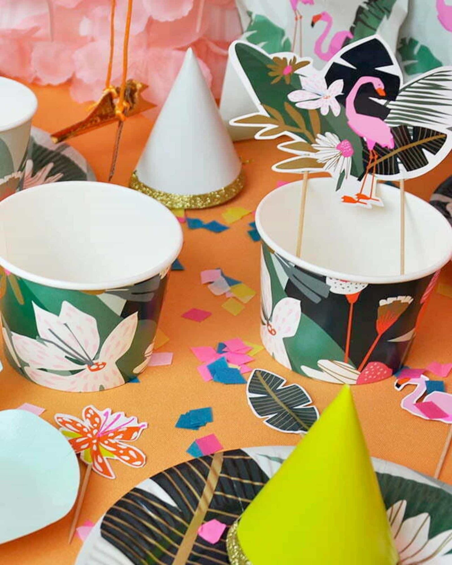 Colorful party scene featuring floral cups, vibrant confetti, and playful flamingo decorations on an orange background.