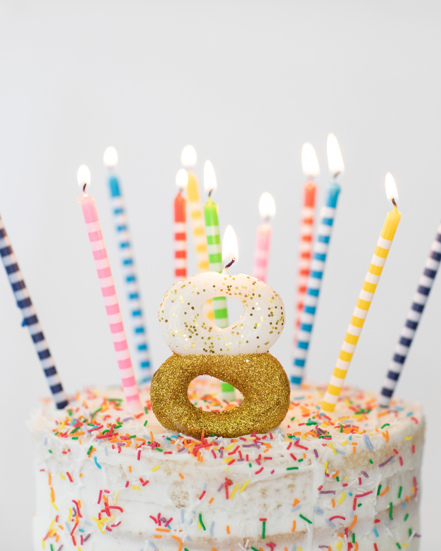 Frosted cake topped with colorful candles and glittery decorations, celebrating a festive occasion.