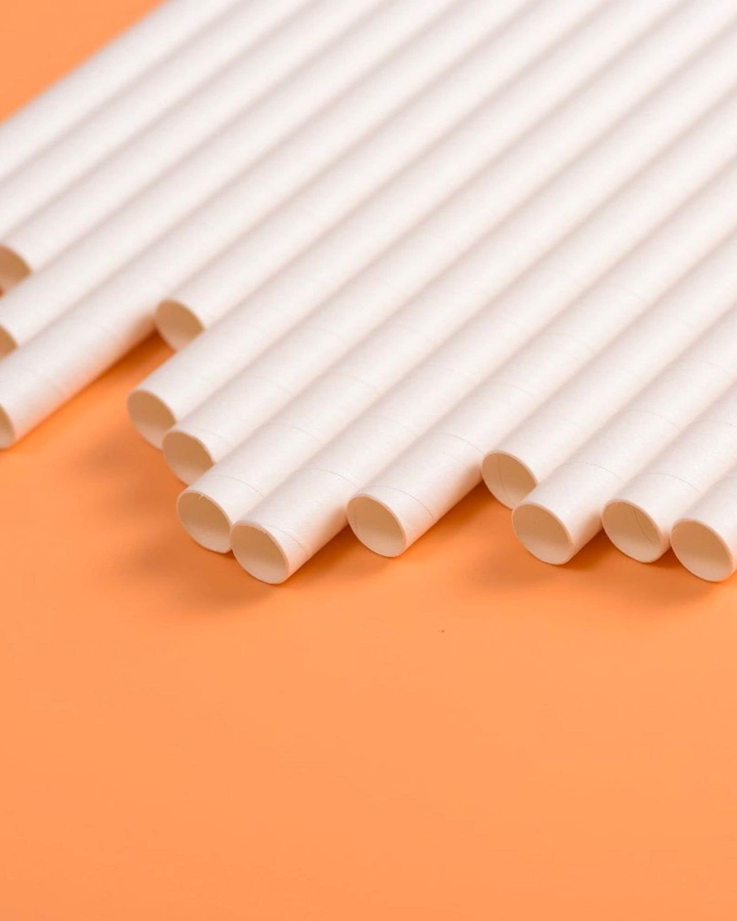 A collection of white cylindrical tubes arranged neatly on a vibrant orange background.