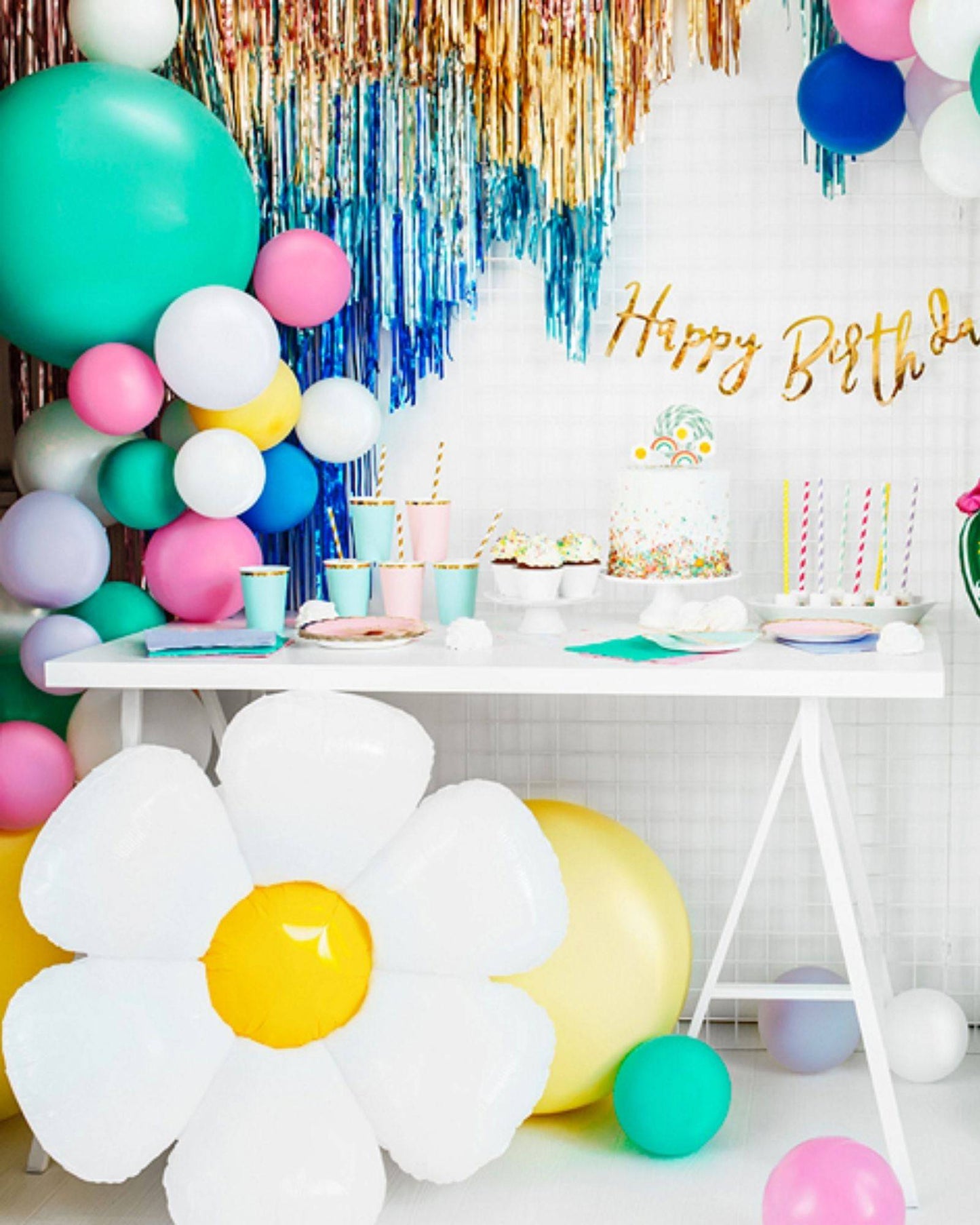 A vibrant birthday setup featuring colorful balloons, a decorated cake, and festive decorations in pastel hues.