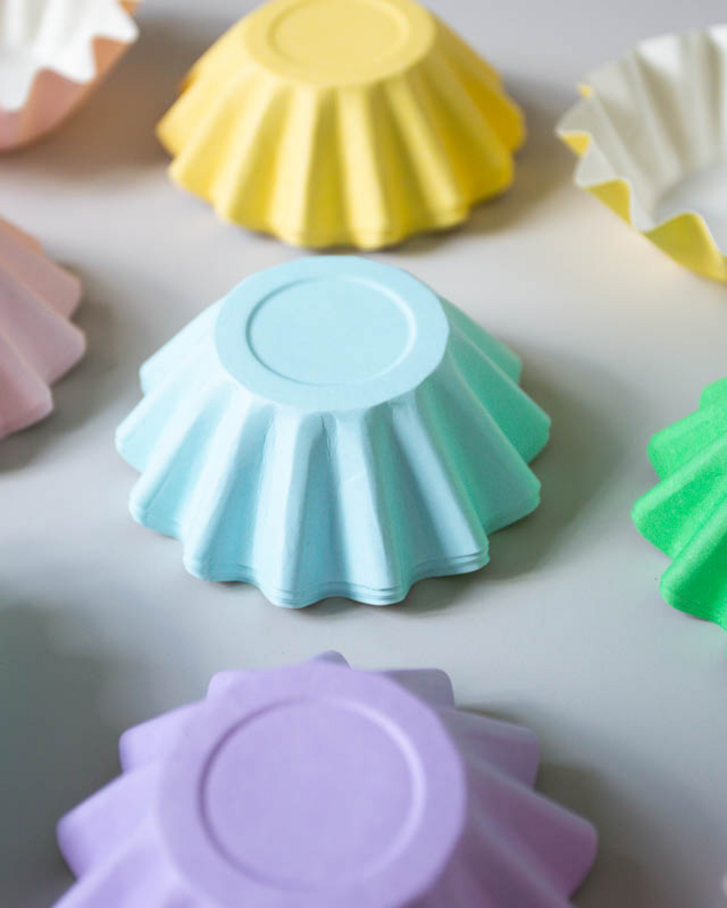 Colorful paper cups in pastel shades of pink, yellow, green, blue, and purple arranged on a light background.