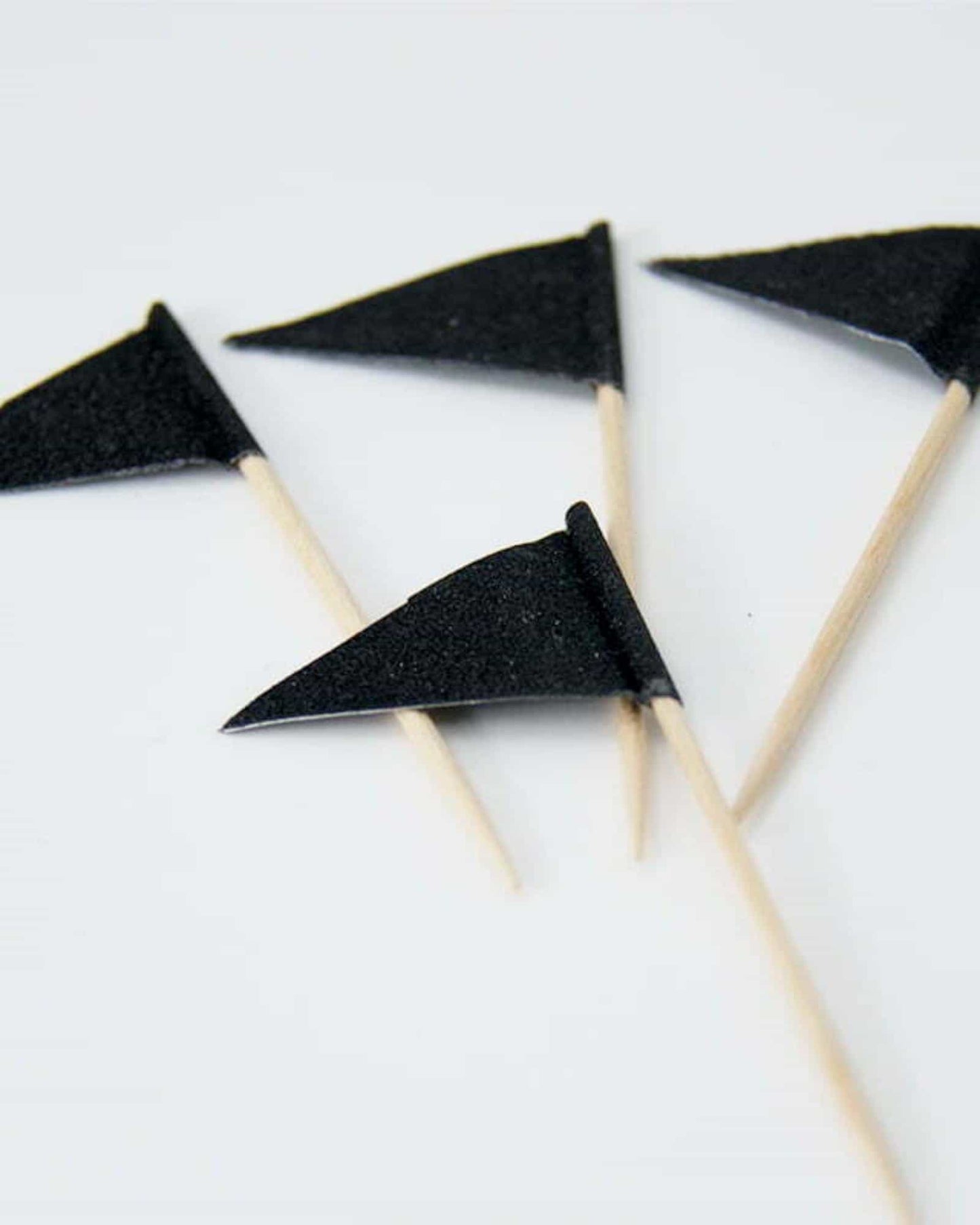 Four small black flags attached to wooden sticks, arranged against a light background.