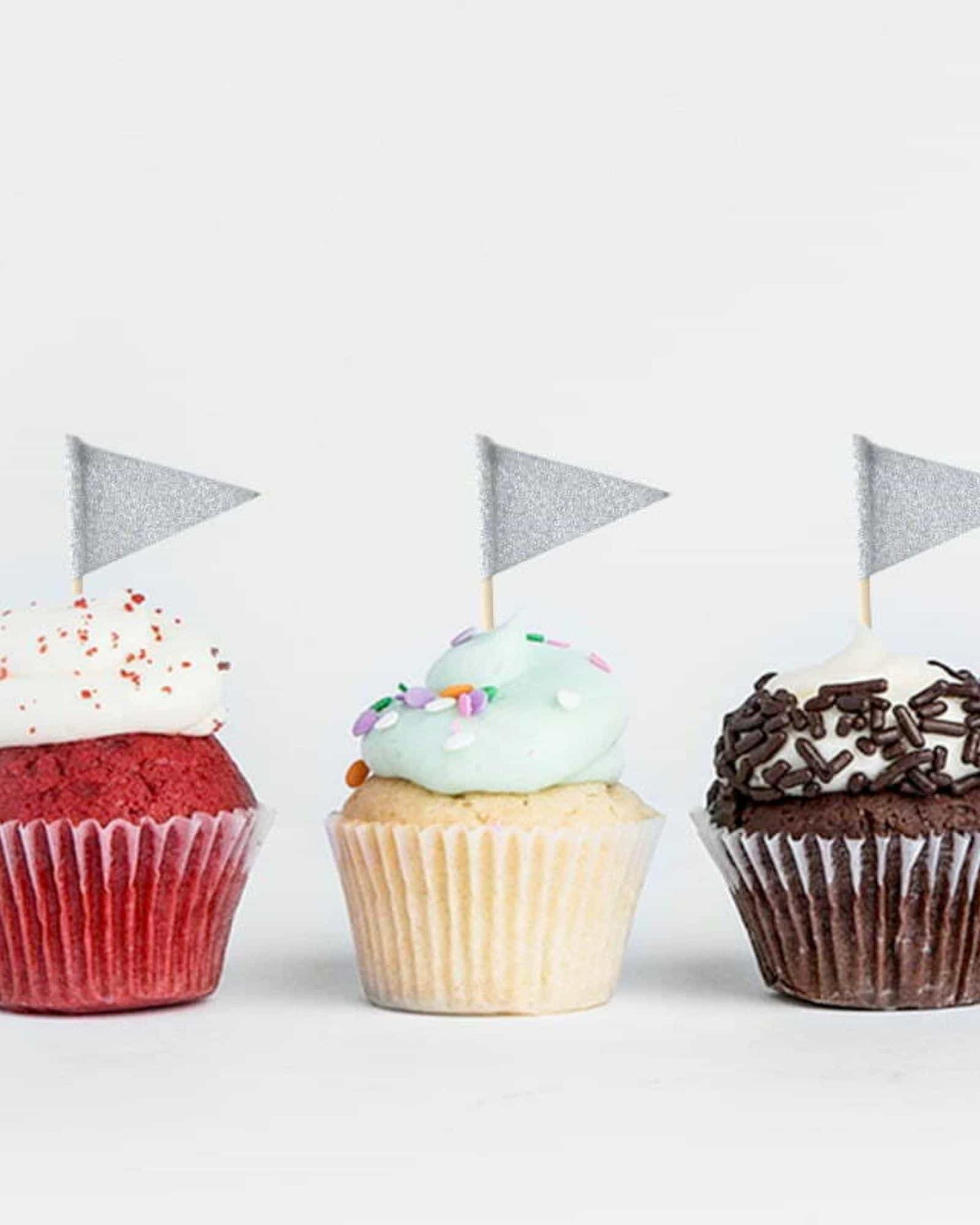 Three colorful cupcakes topped with frosting and decorative flags, arranged on a white background.