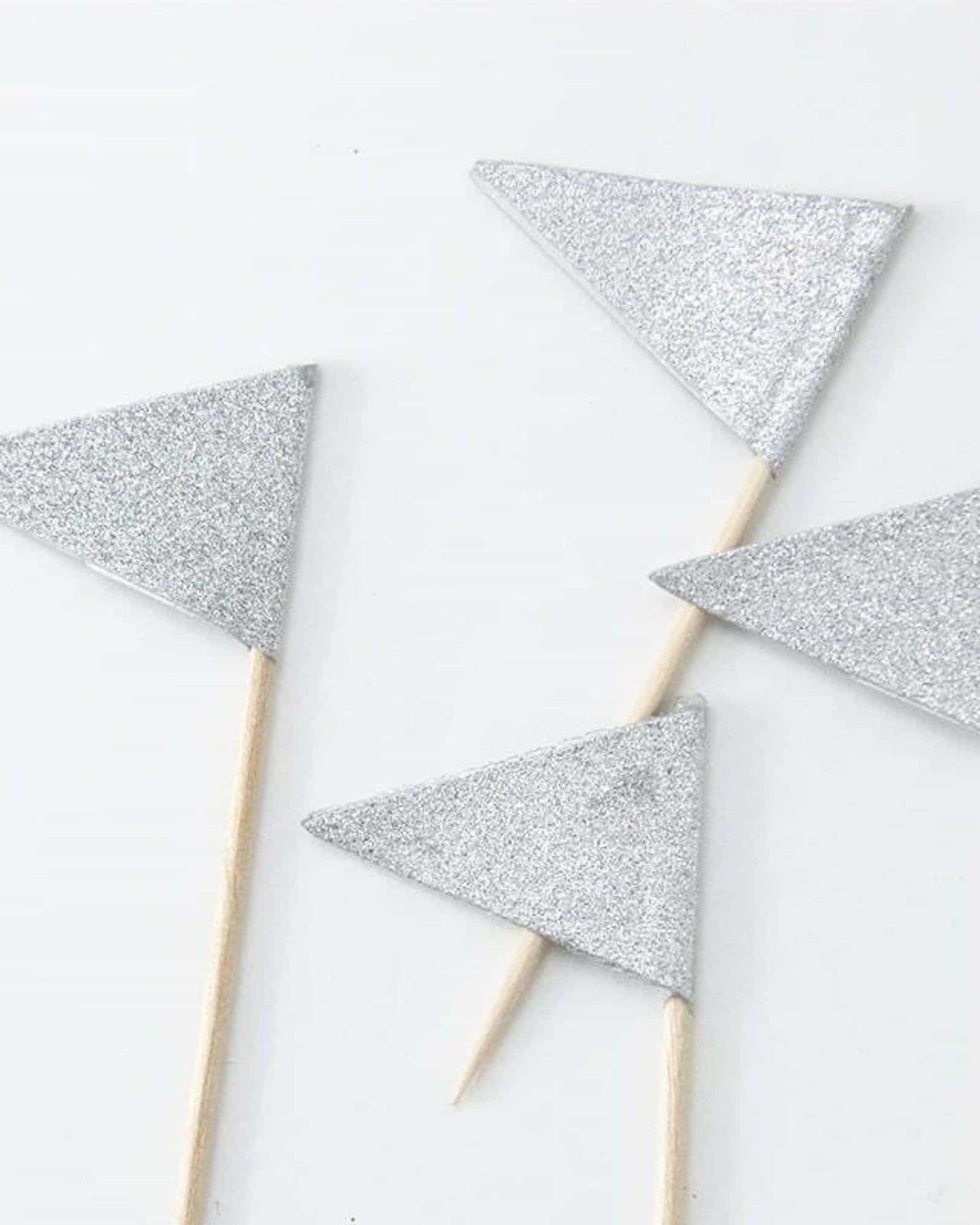 Four small silver glitter triangular shapes attached to wooden sticks on a light background.