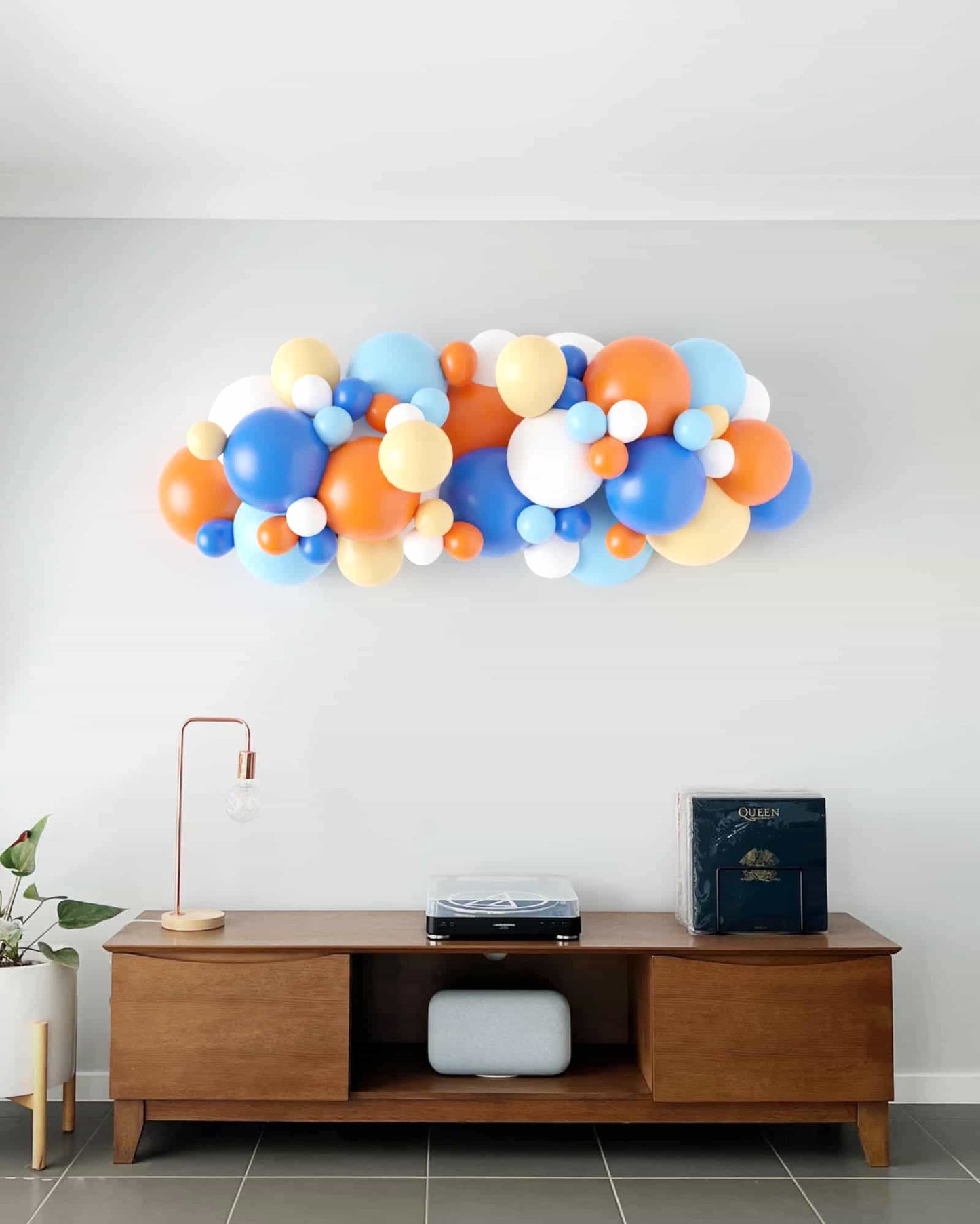 A vibrant garland of blue, orange, yellow, and white balloons decorates a modern interior wall above a stylish wooden console