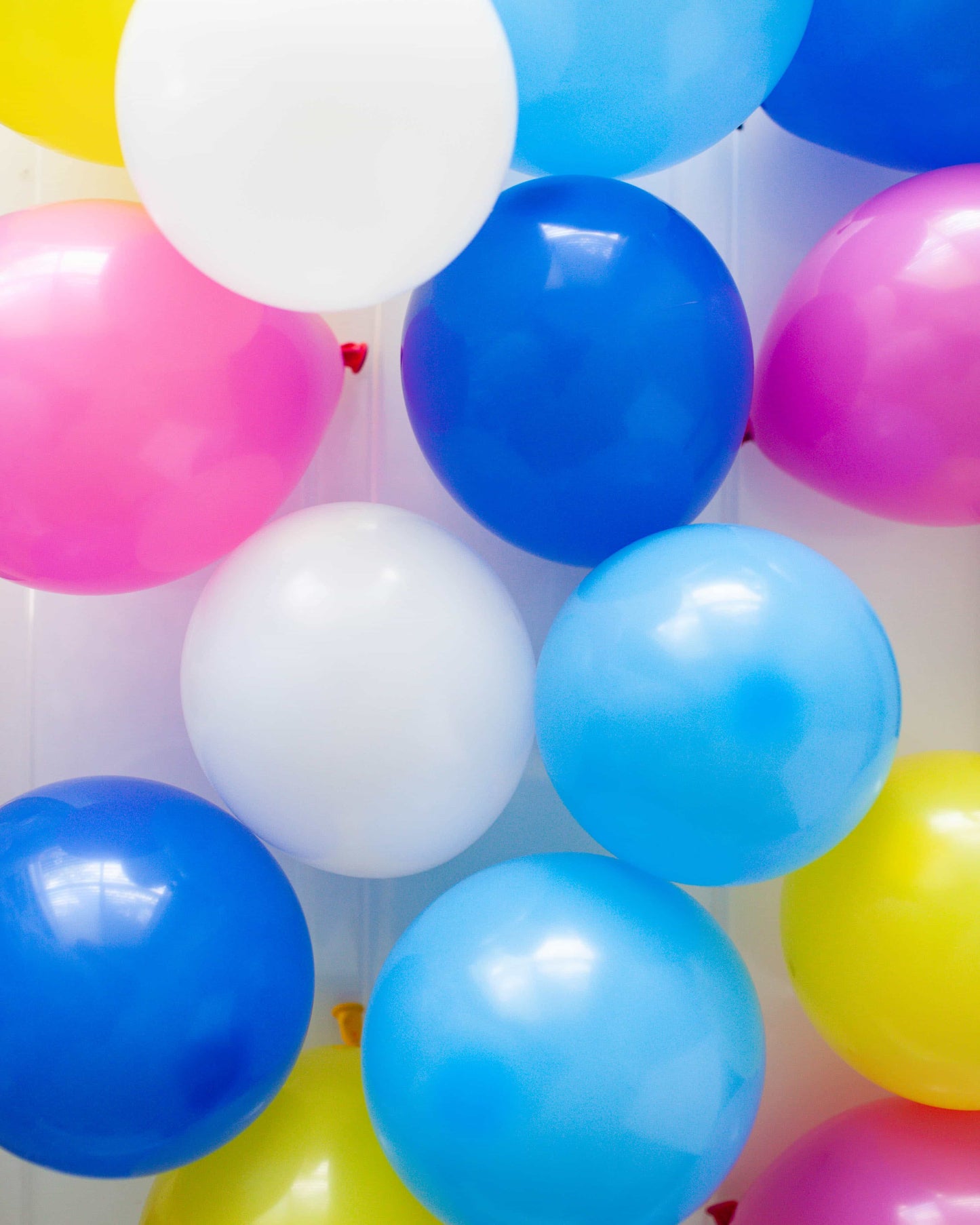 Colorful balloons in pink, blue, yellow, and white arranged closely, creating a festive and cheerful atmosphere.