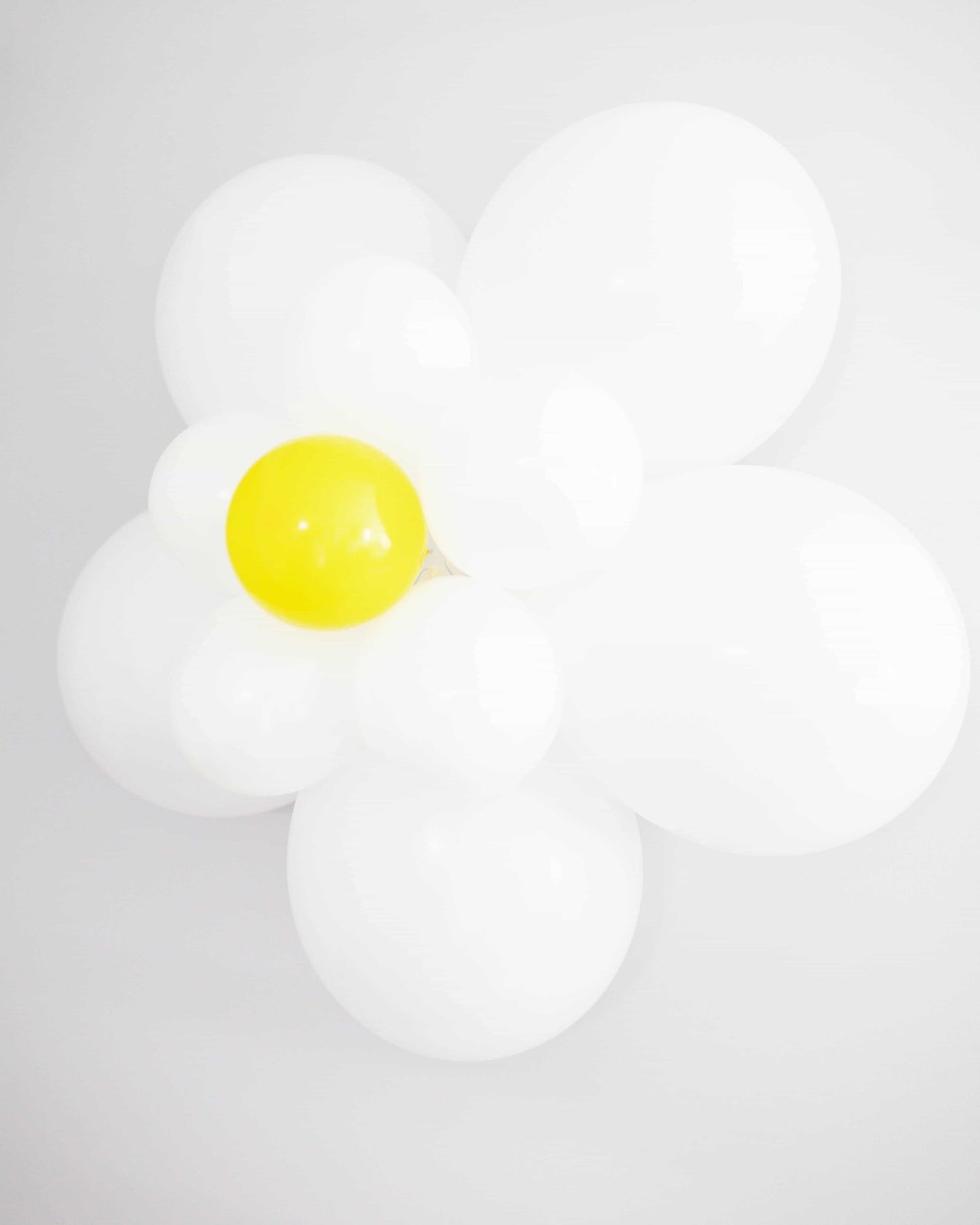 A cluster of white and yellow balloons shaped like a daisy against a plain background, exuding a cheerful vibe.