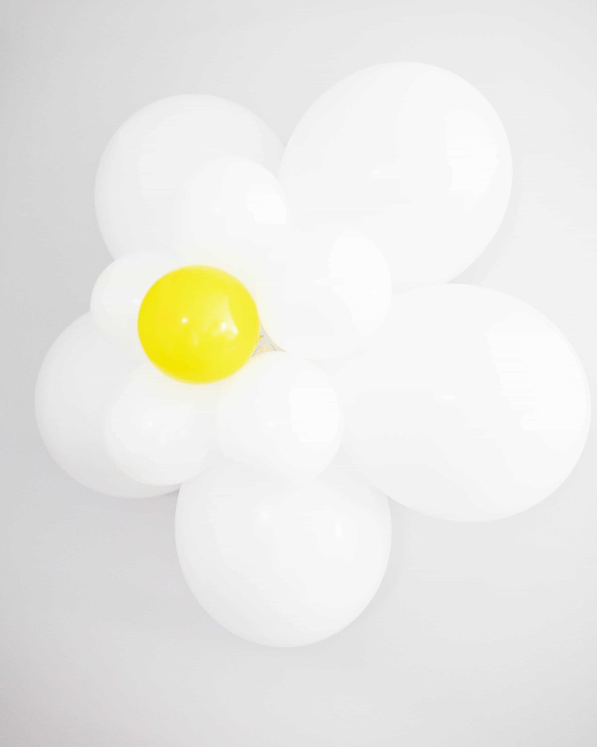 A cluster of white and yellow balloons shaped like a daisy against a plain background, exuding a cheerful vibe.