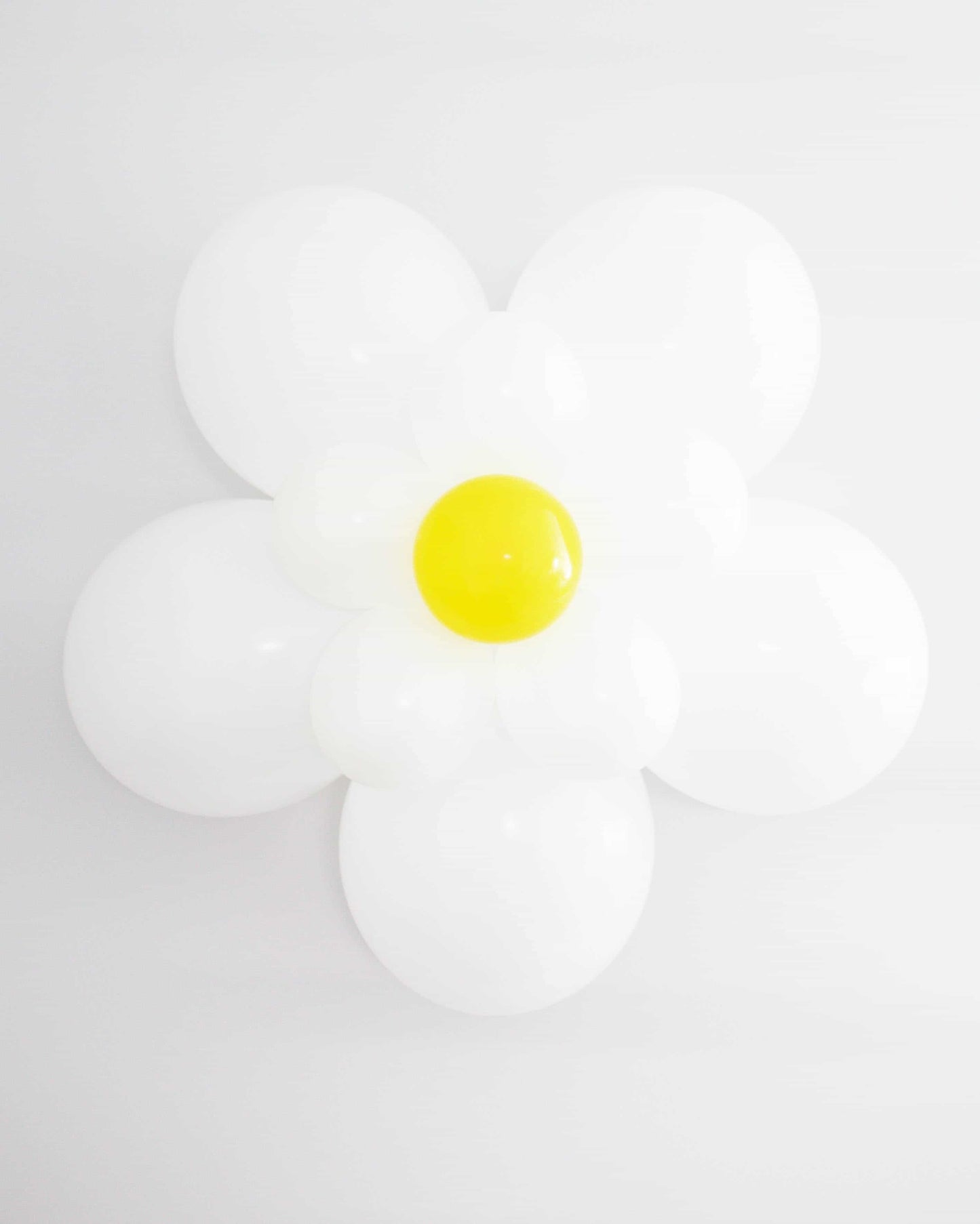 A large, white daisy made of glossy balloons with a bright yellow center against a plain white background.