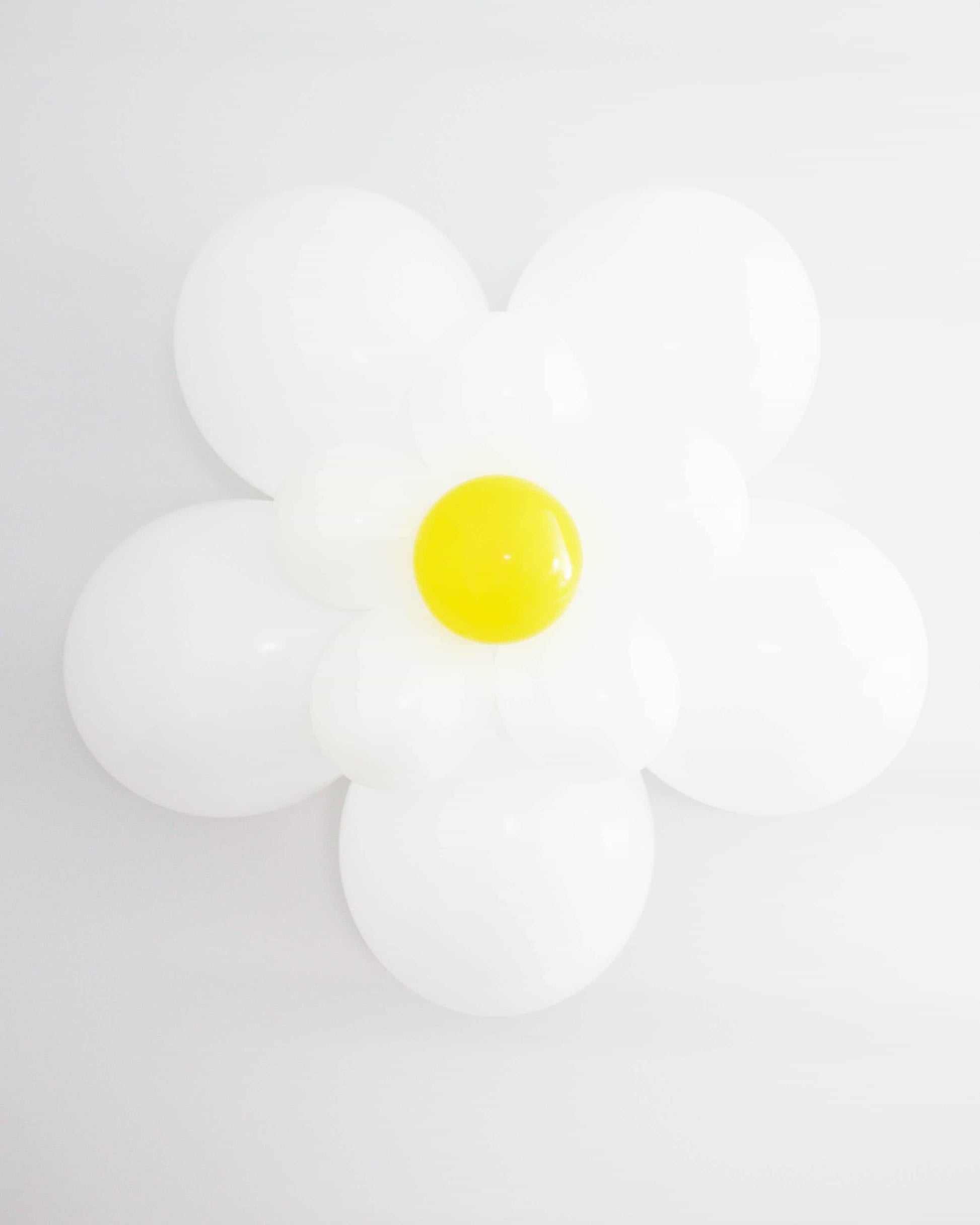 A large, white daisy made of glossy balloons with a bright yellow center against a plain white background.