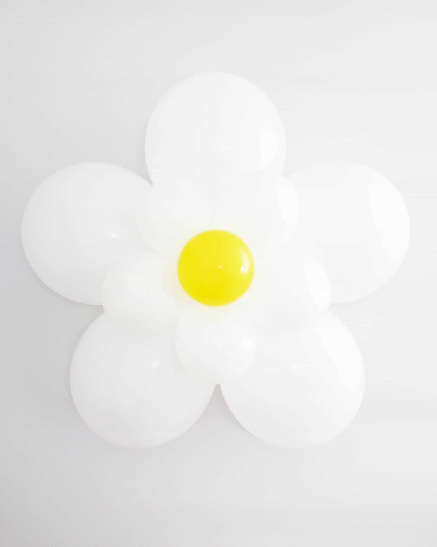 A large, cheerful daisy made of glossy white and bright yellow elements against a soft, neutral background.
