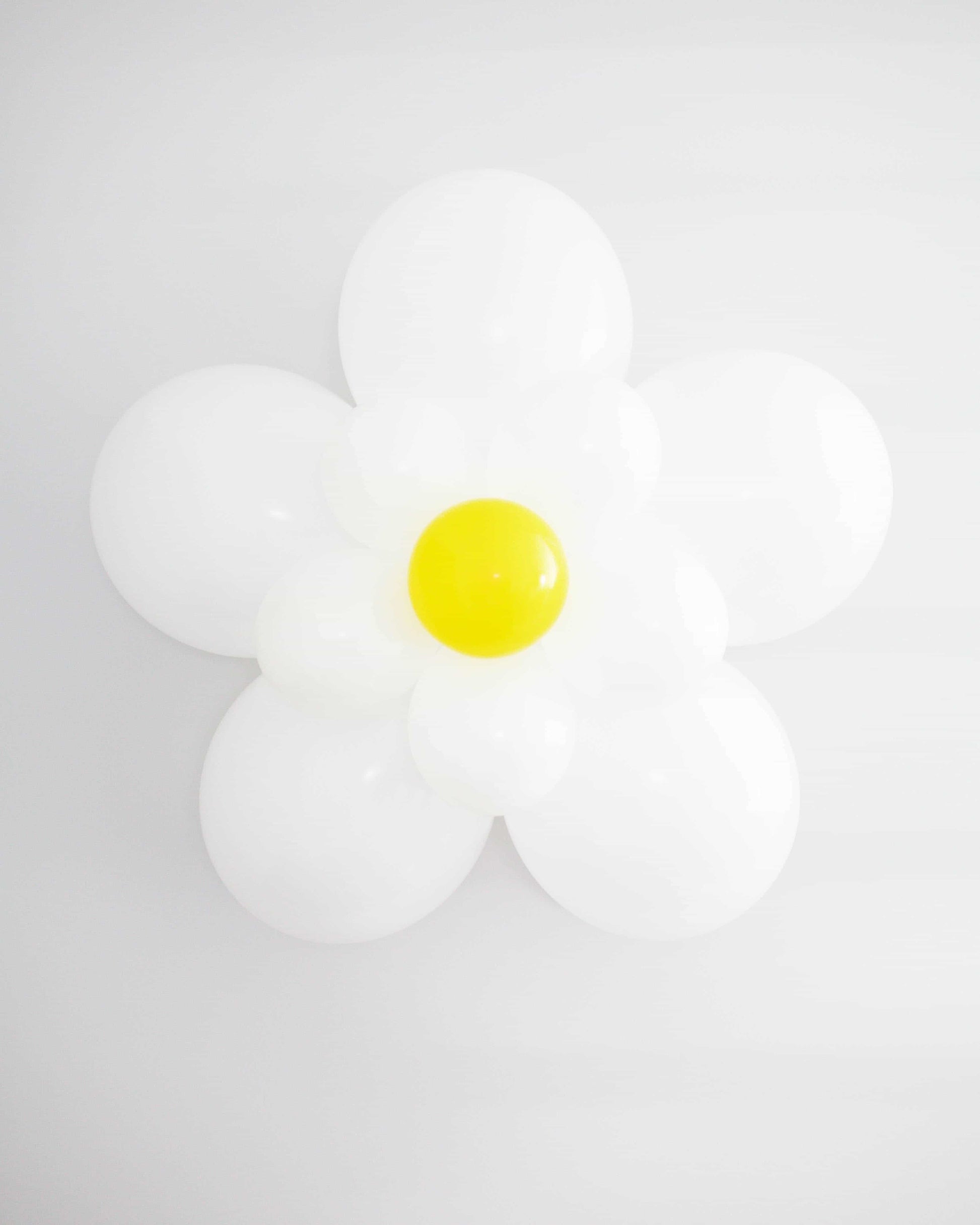A decorative arrangement resembling a daisy, featuring white and yellow rounded elements against a light background.