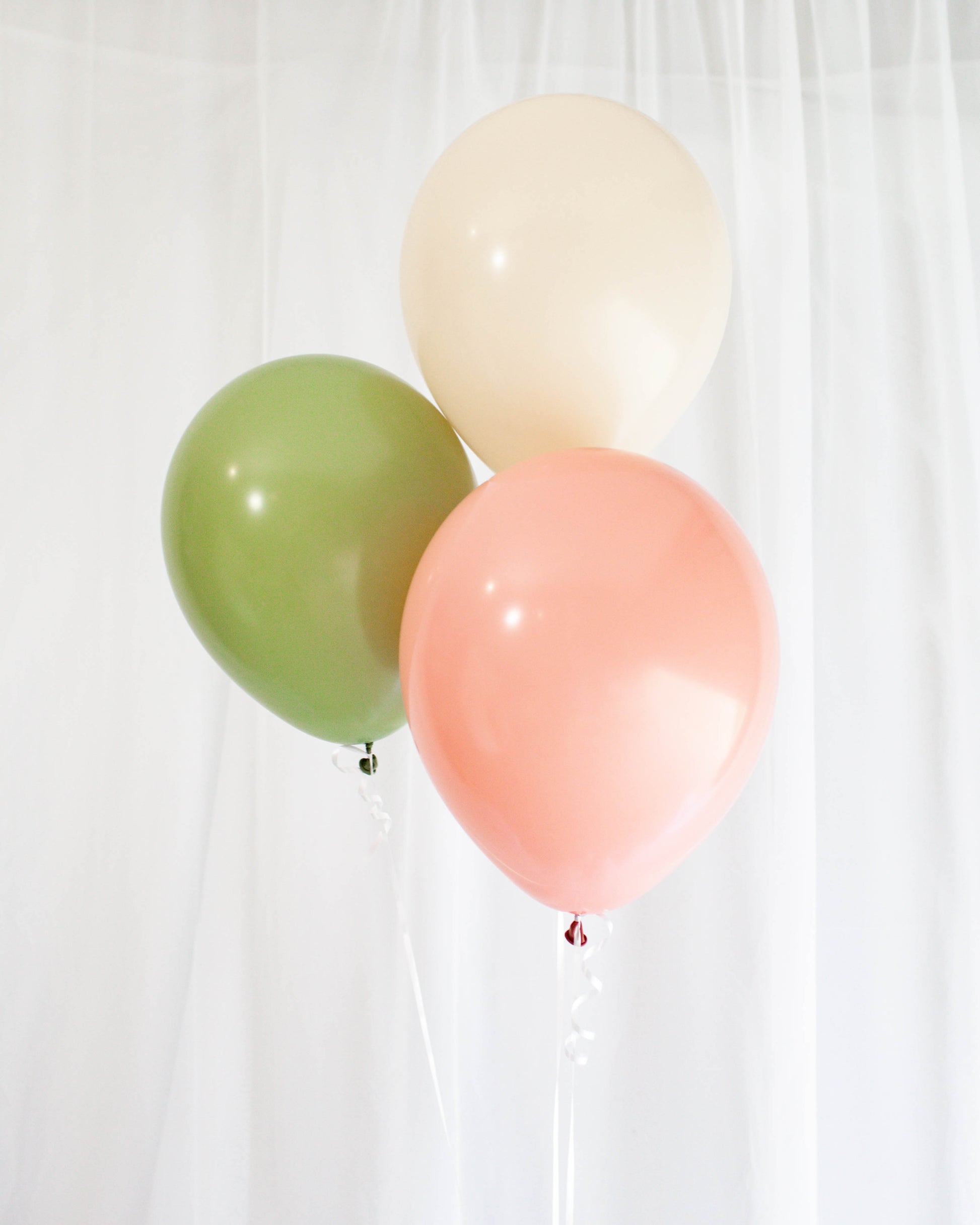 Three balloons in soft hues of pink, cream, and green float against a light backdrop, adding a festive touch.