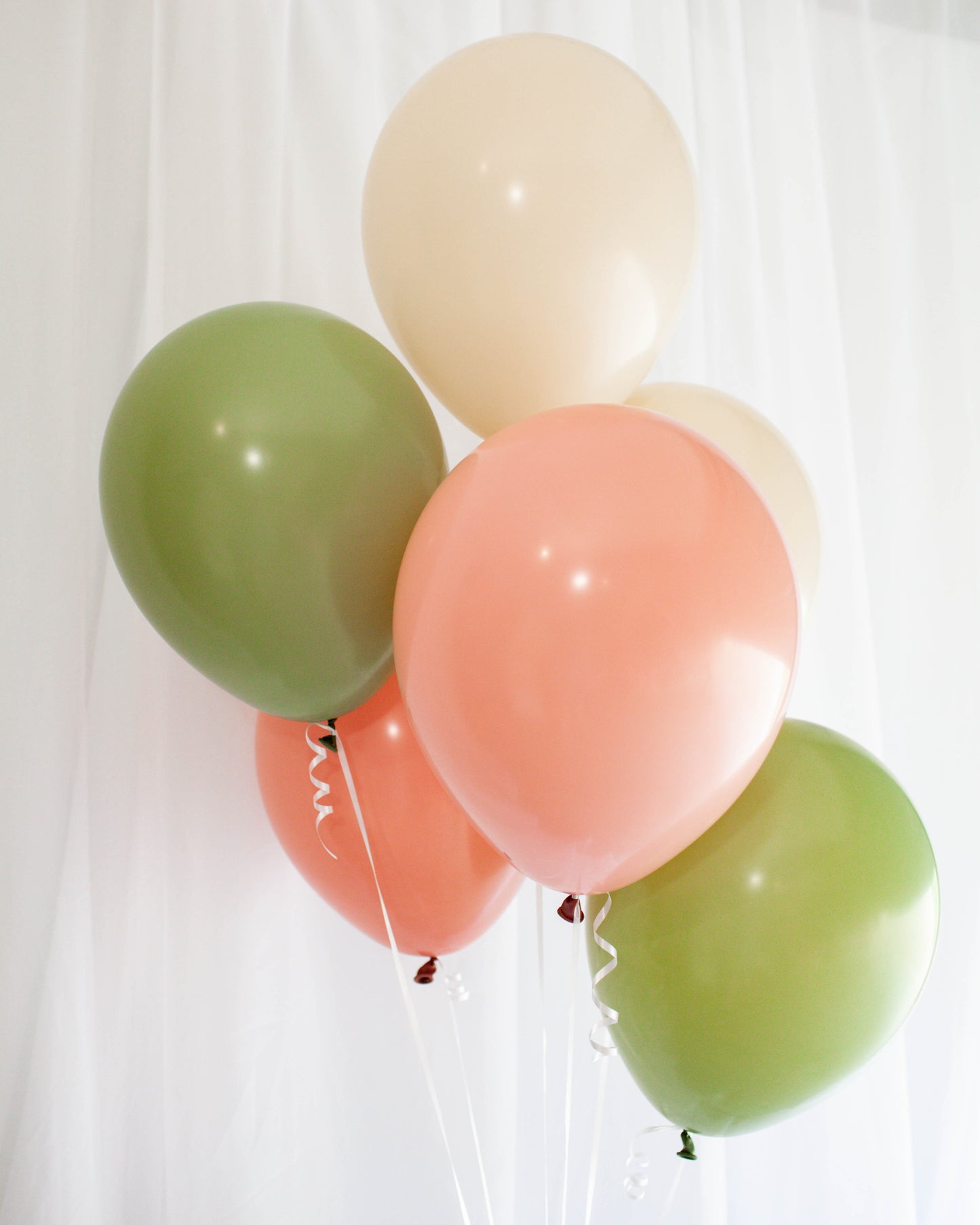 A cluster of pastel balloons in peach, cream, and green, floating against a soft white background.