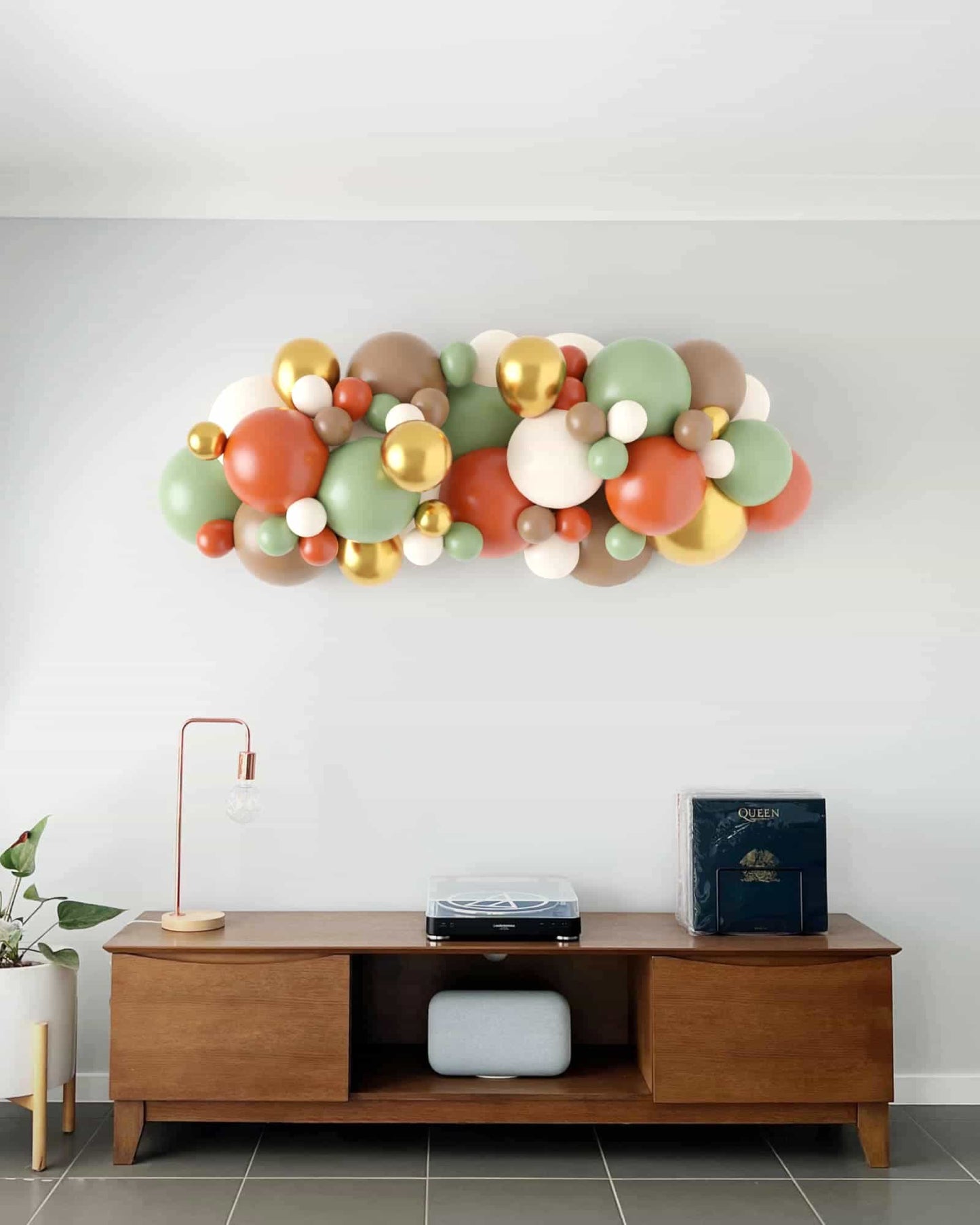 A vibrant arrangement of multicolored balloons in earthy tones, accented with metallic gold, above a wooden console table.