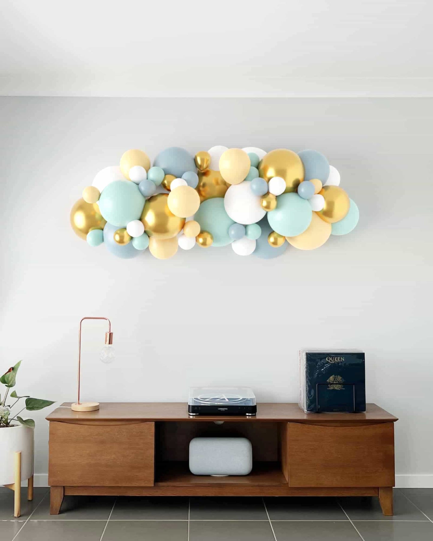 A colorful balloon garland in soft pastels and gold, elegantly arching above a stylish wooden sideboard.