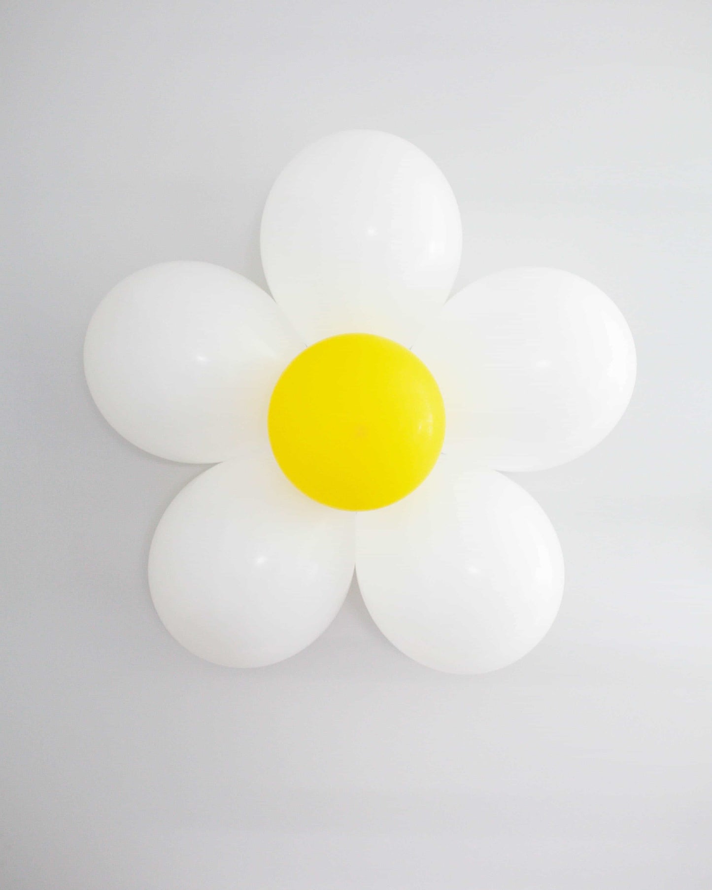 A cheerful daisy made of white and yellow balloons against a light background, adding a whimsical touch to any space.