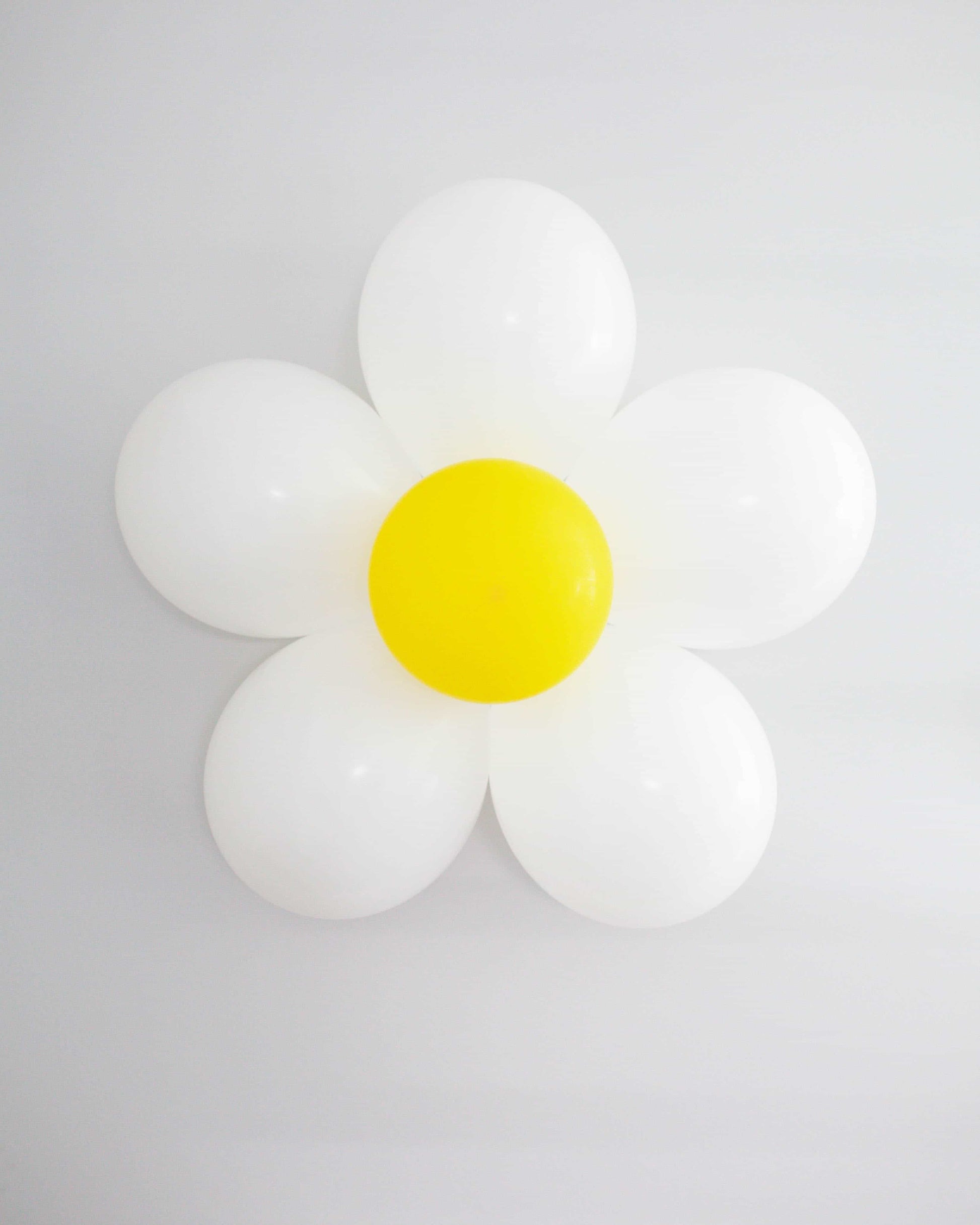 A cheerful daisy made of white and yellow balloons against a light background, adding a whimsical touch to any space.