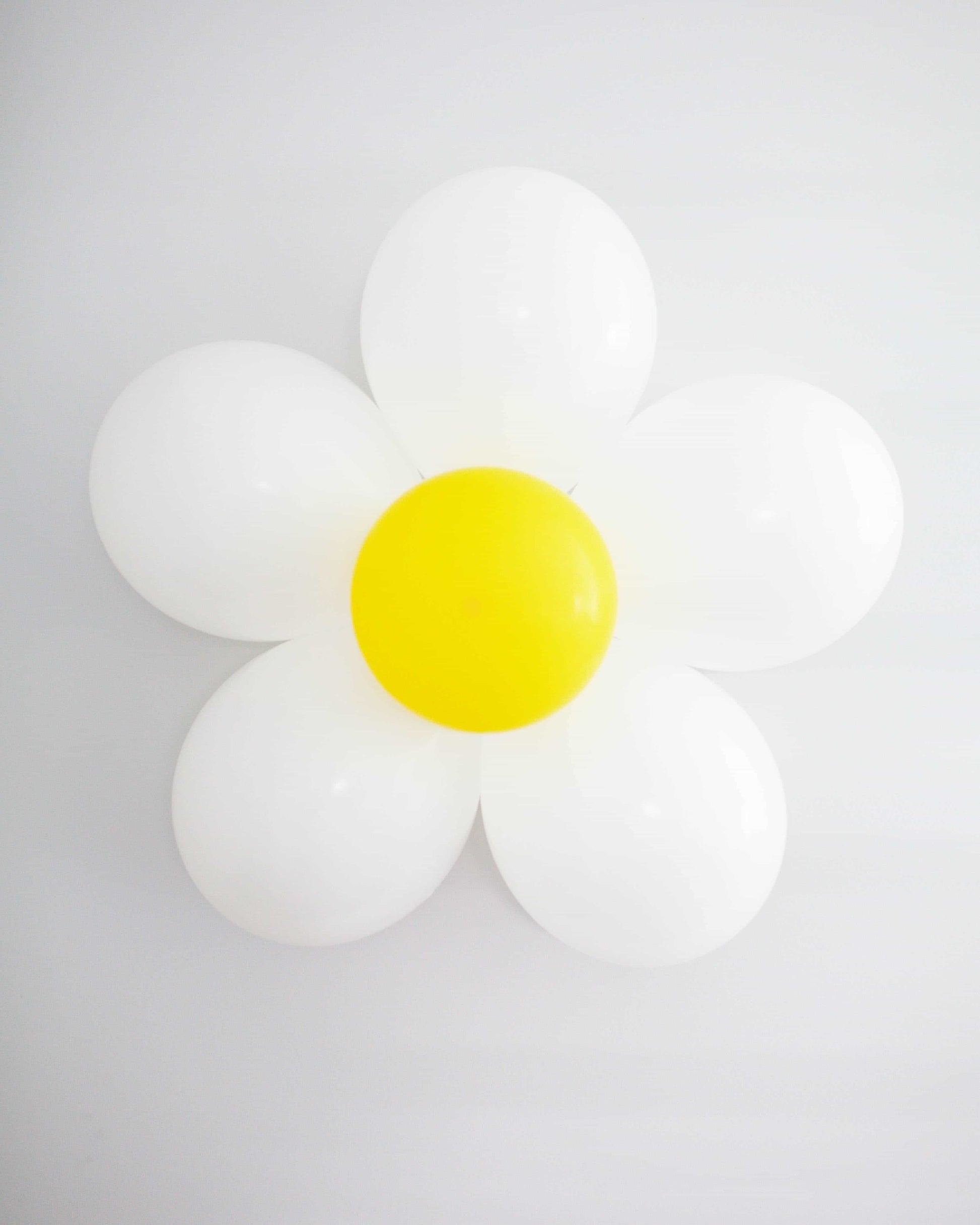 A cheerful arrangement of white balloons shaped like a daisy, featuring a vibrant yellow center against a light background.