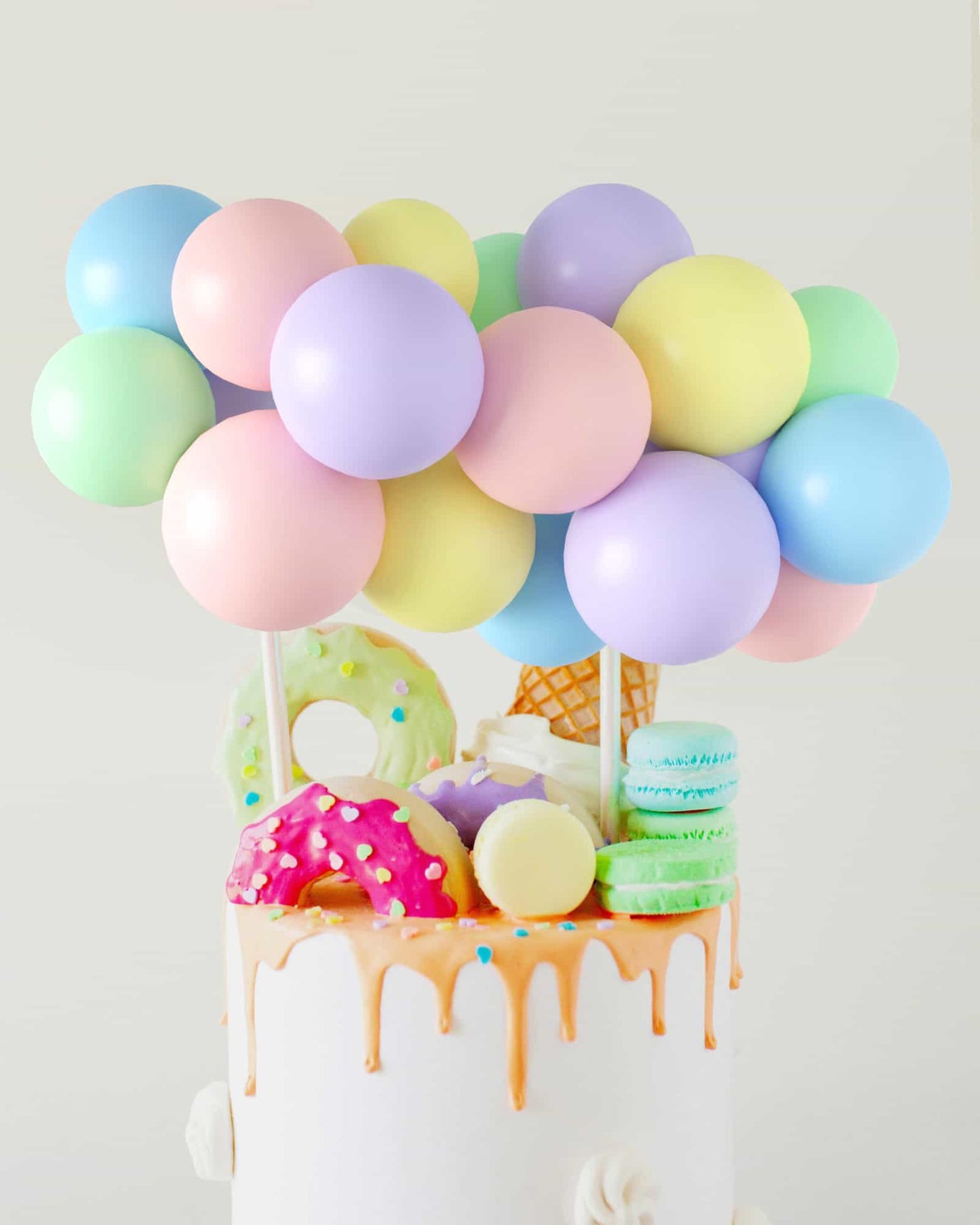 A whimsical cake topped with pastel balloons and colorful, decorative treats, creating a festive atmosphere.