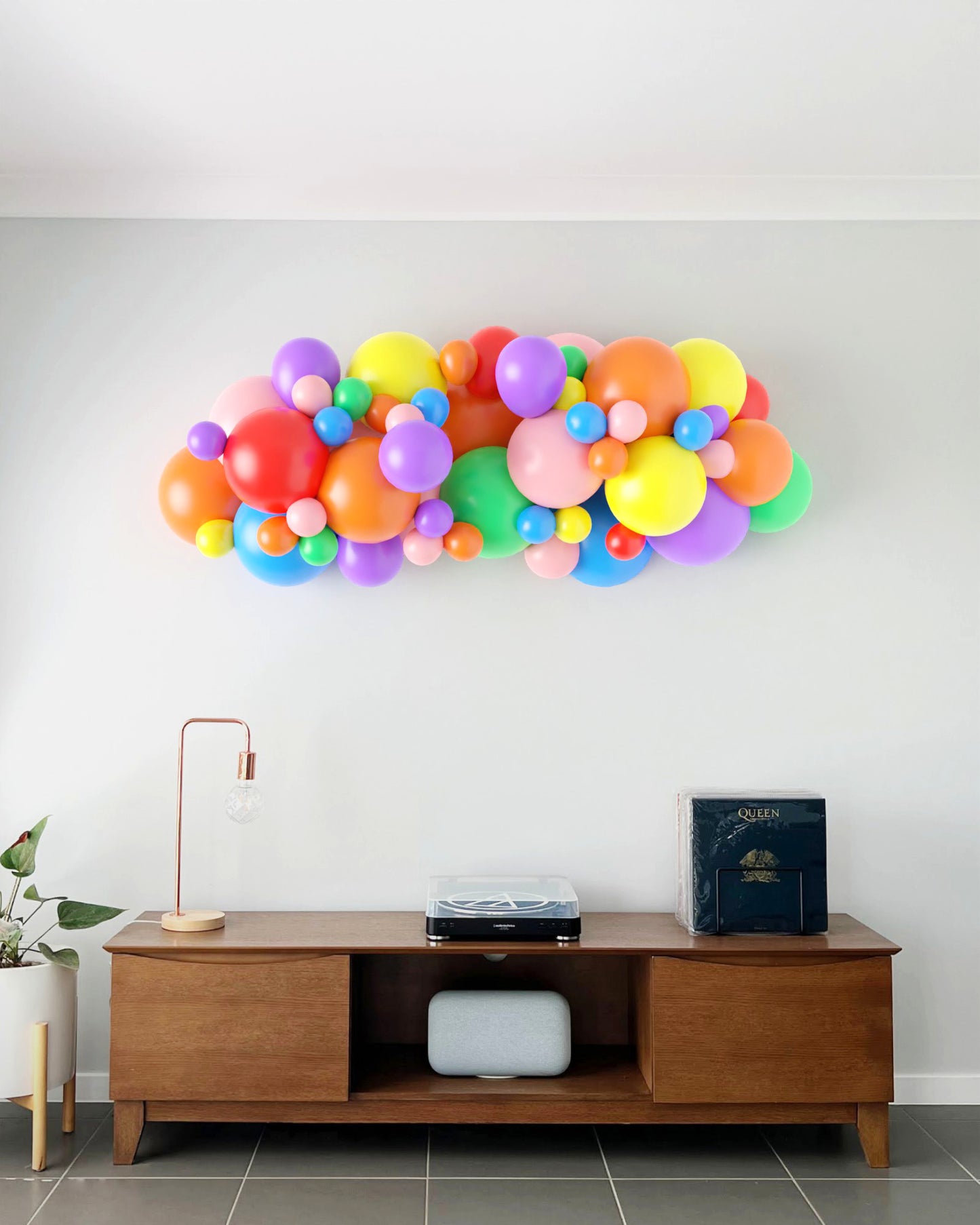 Colorful balloon garland featuring various sizes and shades, mounted on a light wall above a wooden console table.